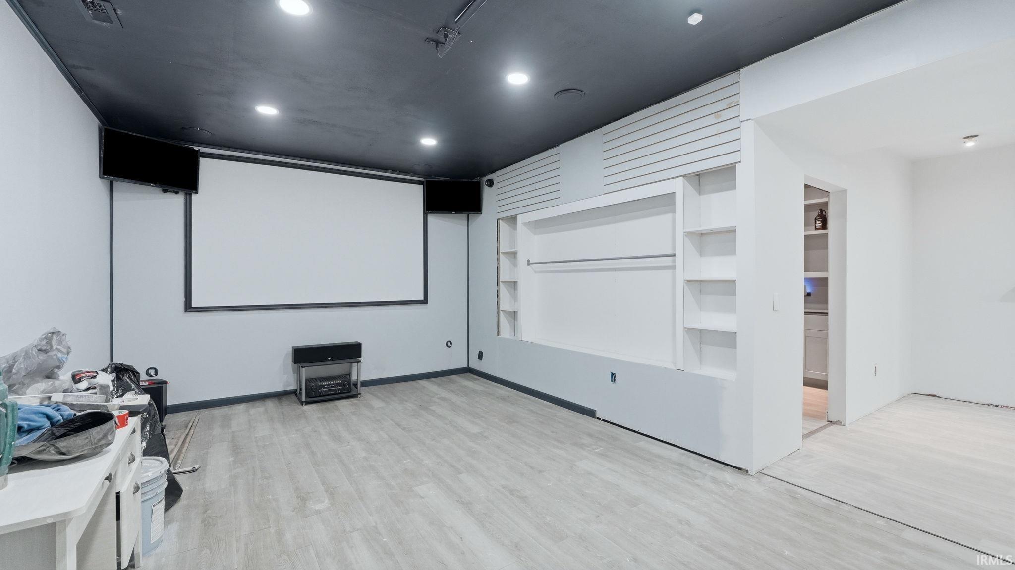 Entertainment room featuring a large projection screen, built-in media center with shelving, recessed lighting, wood-finish flooring, and a dark ceiling