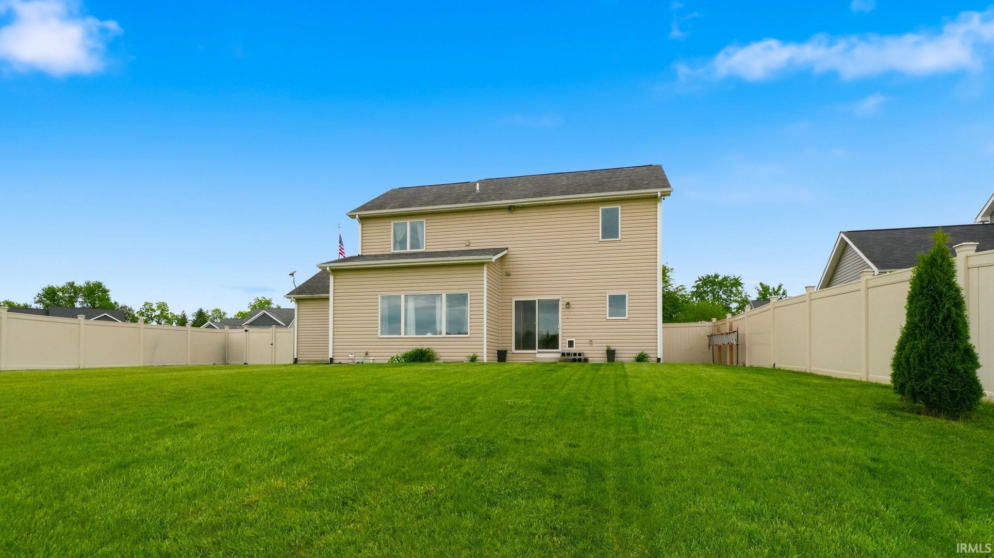 Expansive rear yard featuring a large green lawn, full vinyl privacy fencing, and a two-story residence with tan siding and a sliding glass door