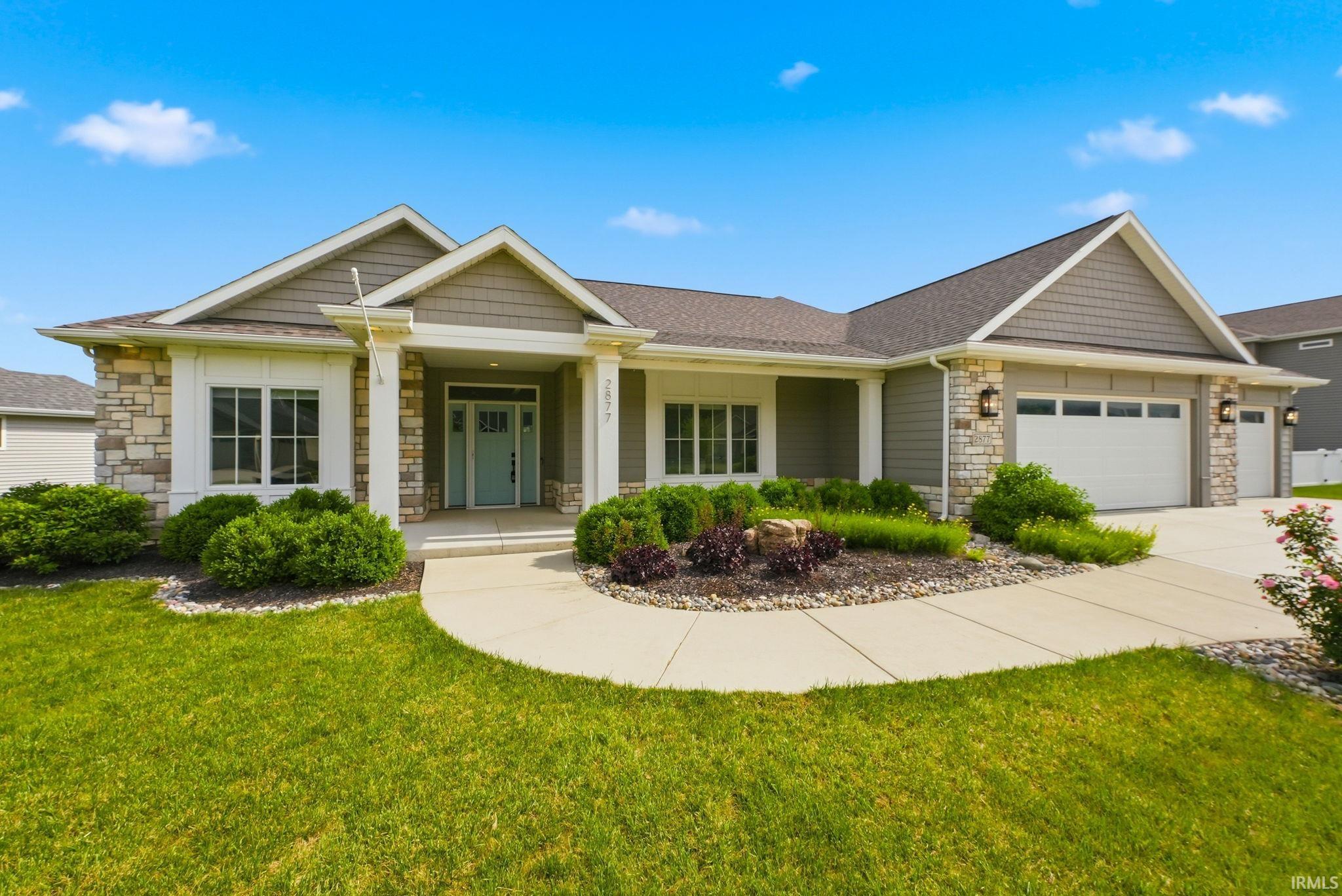 Ranch-style residence featuring a stone and siding exterior, an inviting covered entry, and a multi-car garage