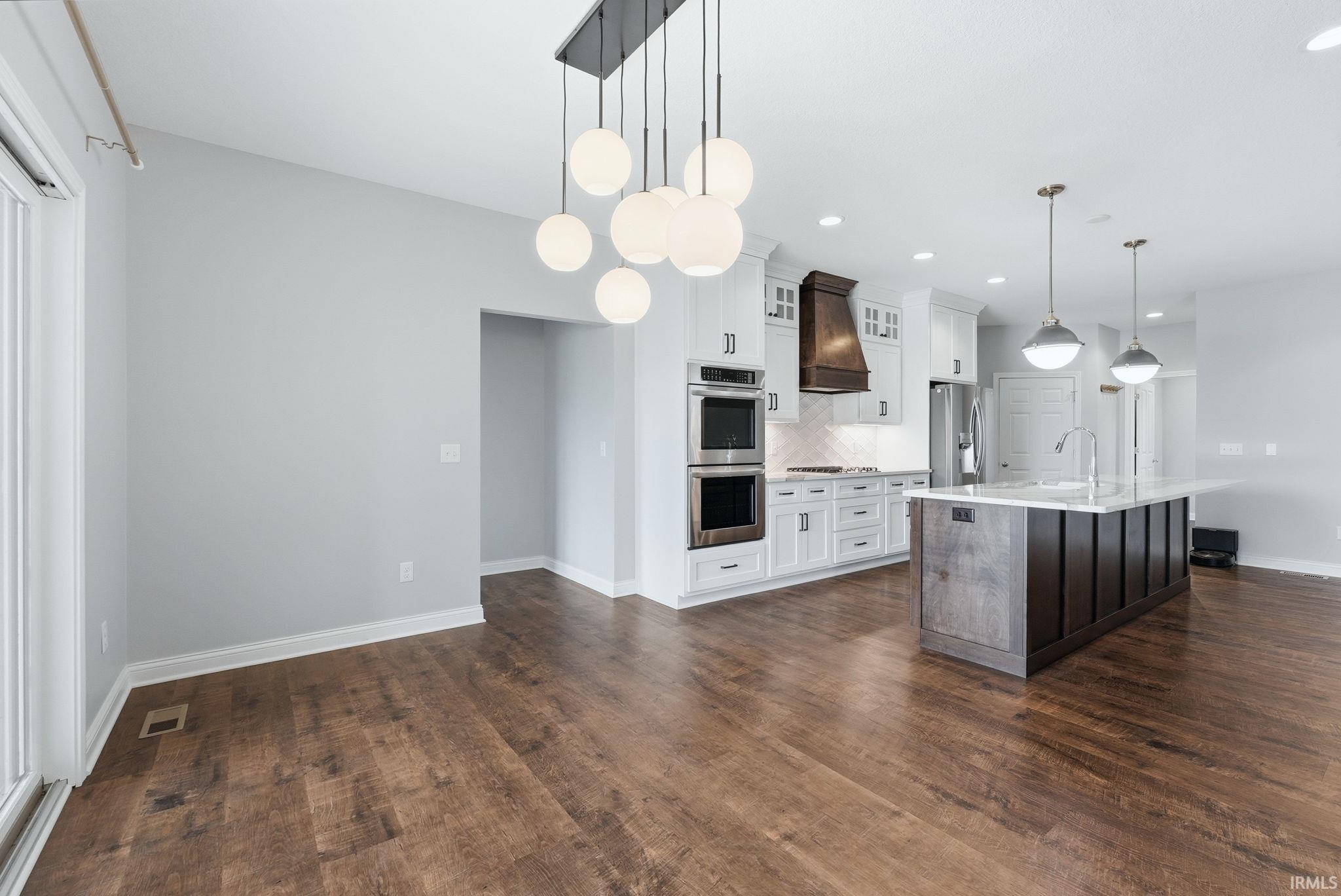 Open-concept living area featuring wood-finish flooring, a contemporary chandelier, and a kitchen with white cabinetry, stainless steel appliances, and a large central island with pendant lighting