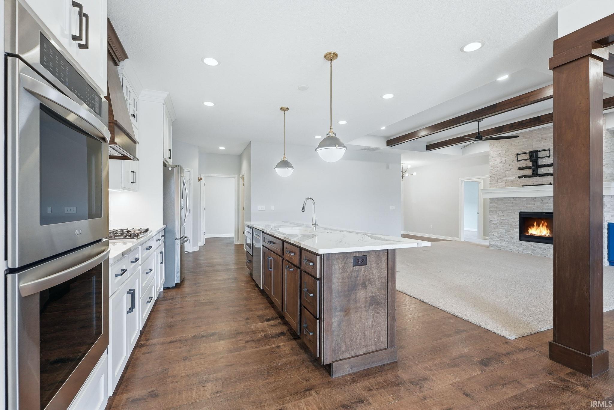 Gourmet kitchen featuring stainless steel appliances, a center island with a sink, white cabinetry, and wood-finish flooring