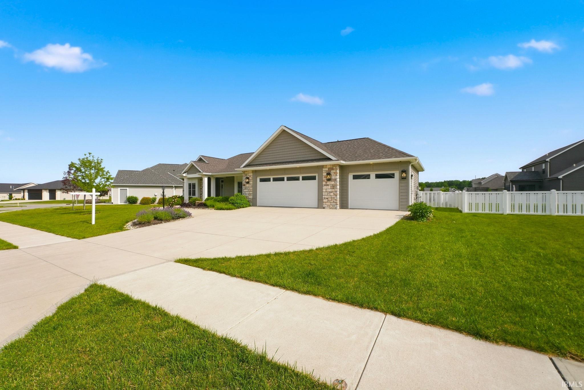 Ranch-style residence featuring a combination of siding and stone veneer, an attached triple-bay garage with white doors, a concrete driveway, and a white picket fence enclosing a portion of the yard