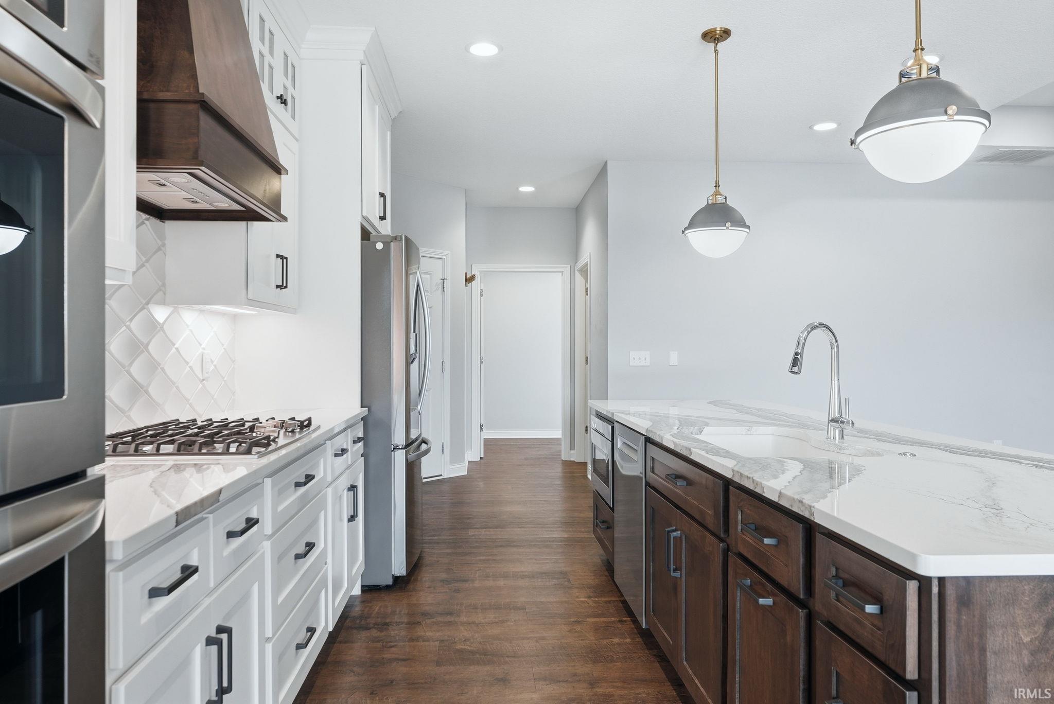 Open-concept kitchen featuring white shaker cabinetry, stainless steel appliances, a gas range with a wood-finish range hood, and an oversized island with a gooseneck faucet