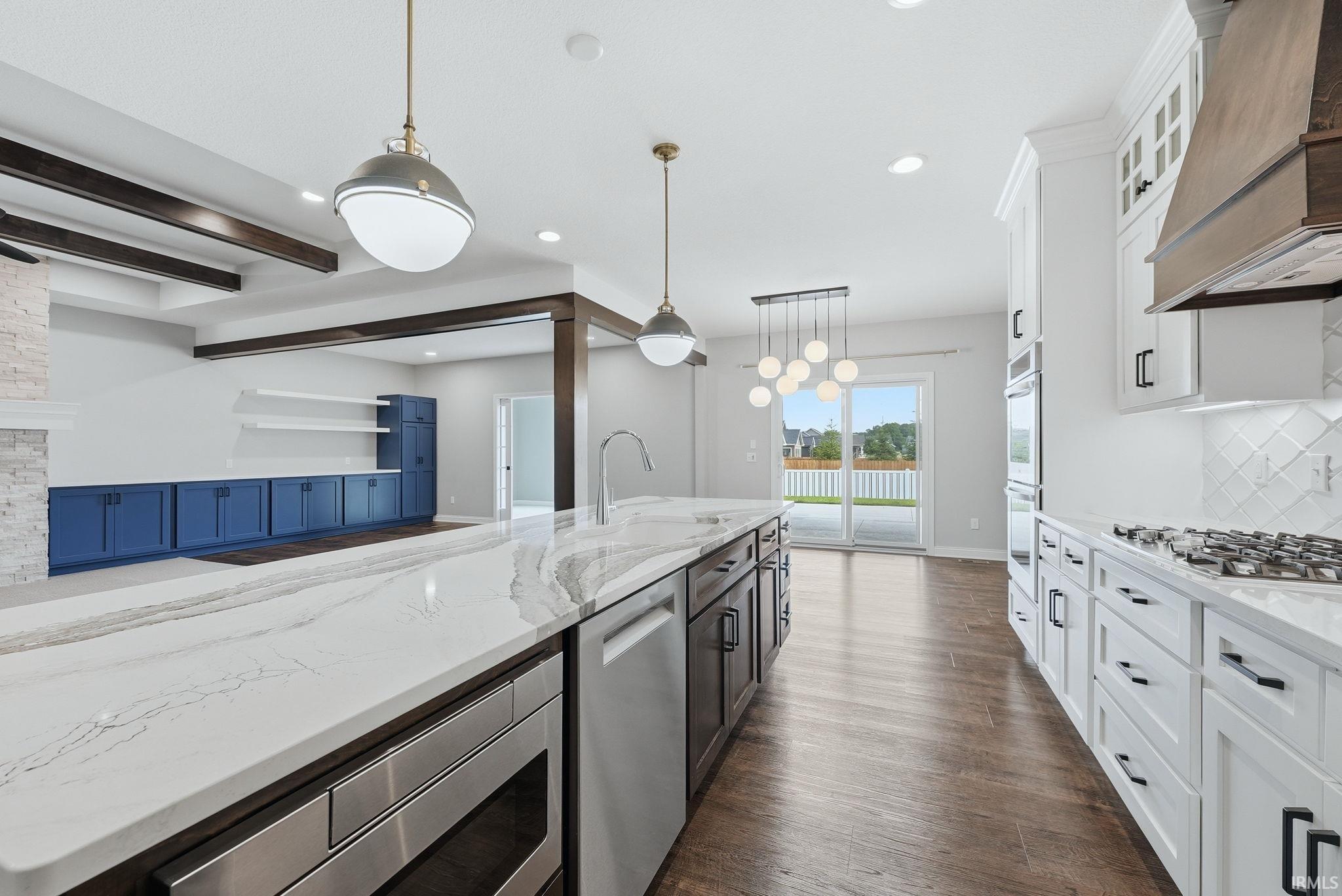 Gourmet kitchen featuring a large central island with integrated microwave, stainless steel appliances, white cabinetry with dark hardware, and wood-finish flooring