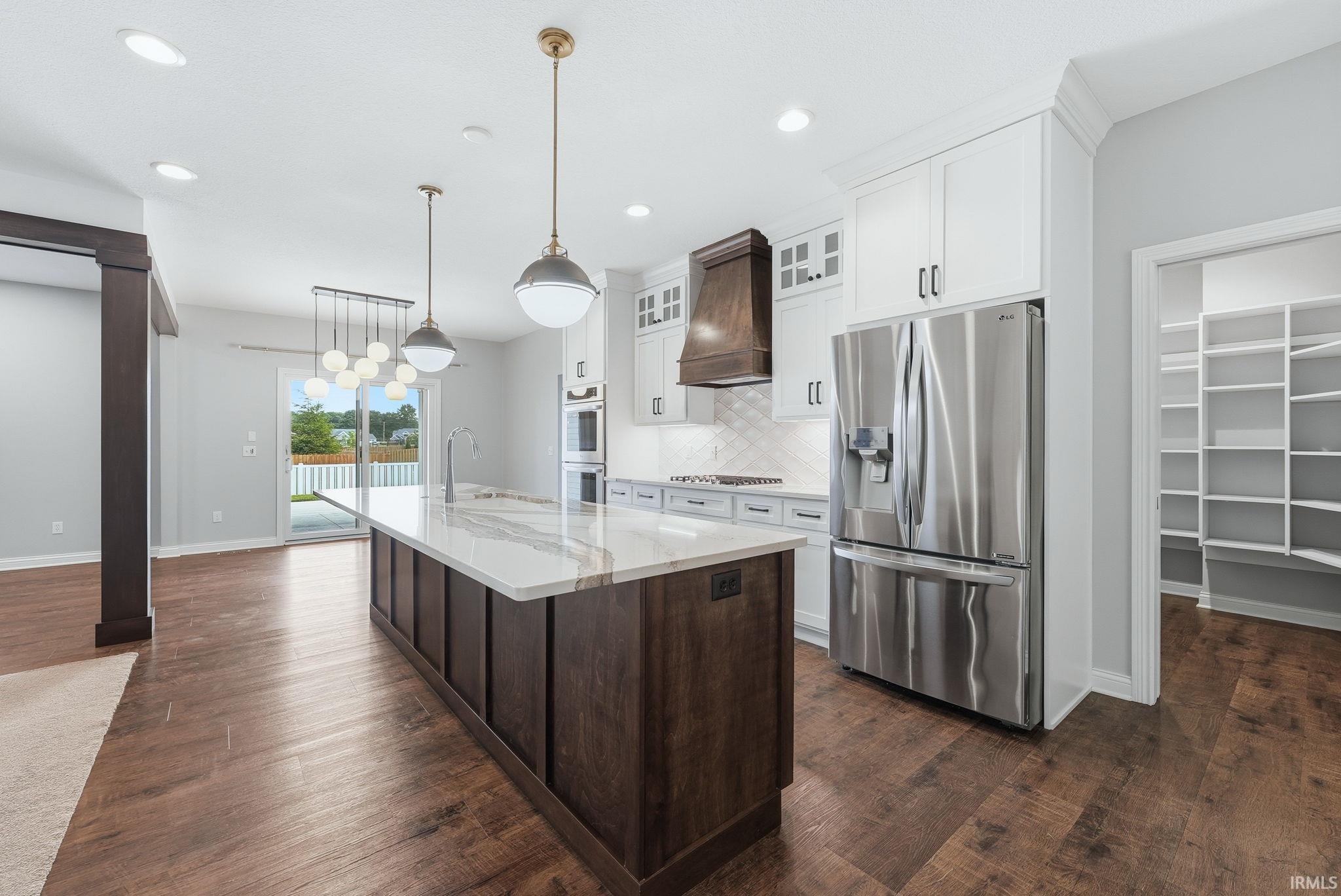 Modern kitchen featuring a large island with a light-toned countertop, stainless steel appliances, white cabinetry, and wood-finish flooring