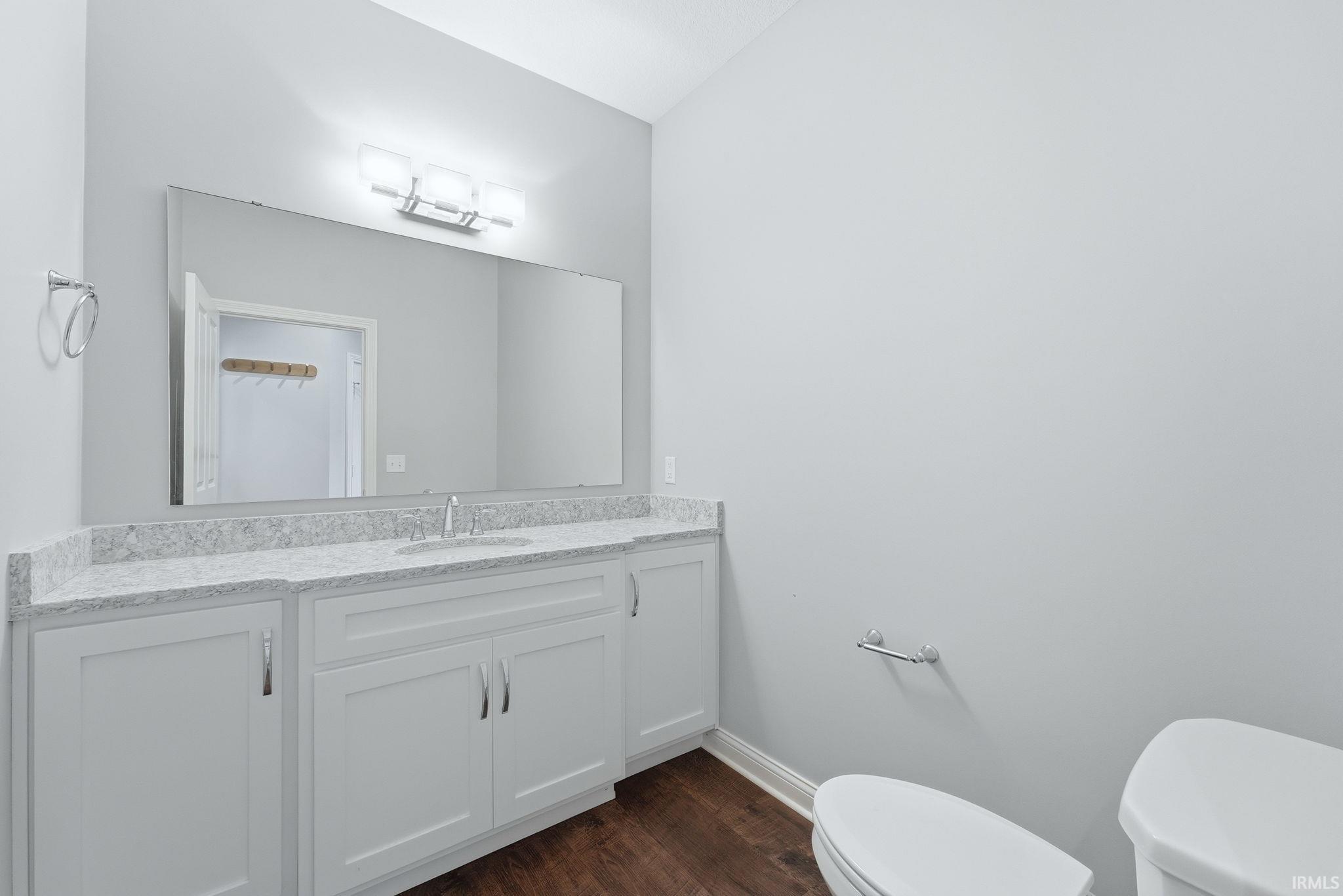 Bathroom featuring white cabinetry, a light-toned countertop, a wide mirror, and rich wood-finish flooring