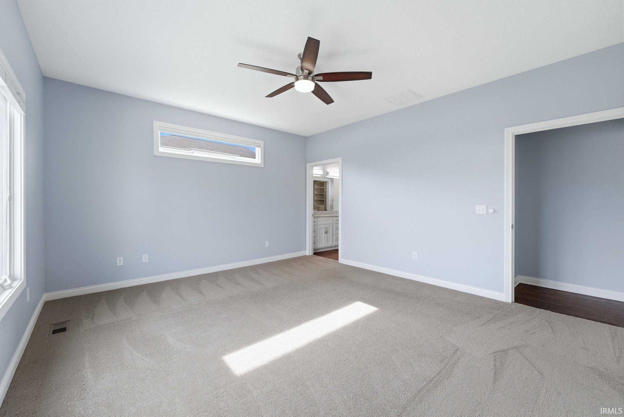 Spacious room featuring light blue walls, neutral carpeting, a ceiling fan, and multiple windows for natural light