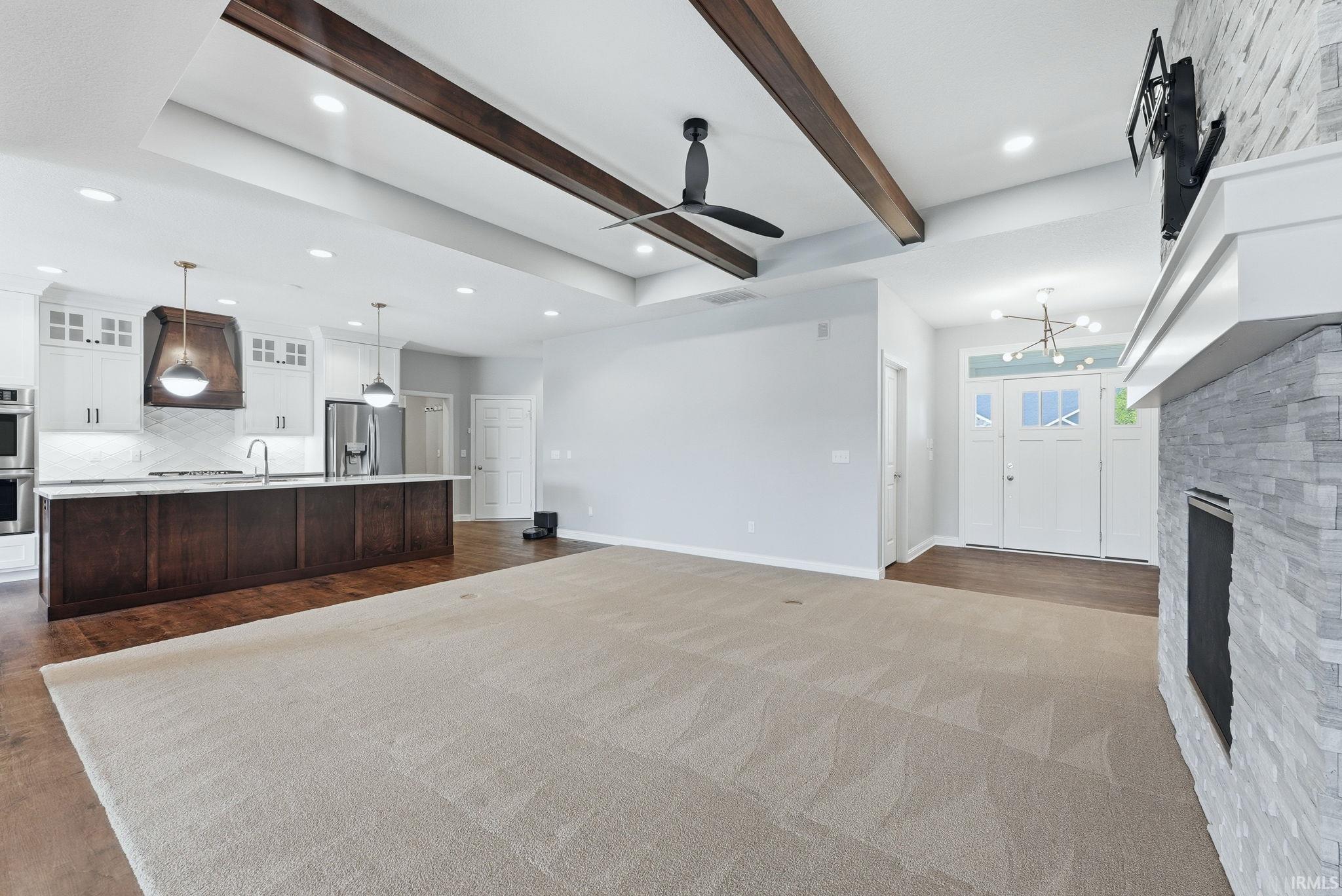Expansive open-concept living space featuring a fireplace with stacked stone surround, dark wood ceiling beams, and recessed lighting