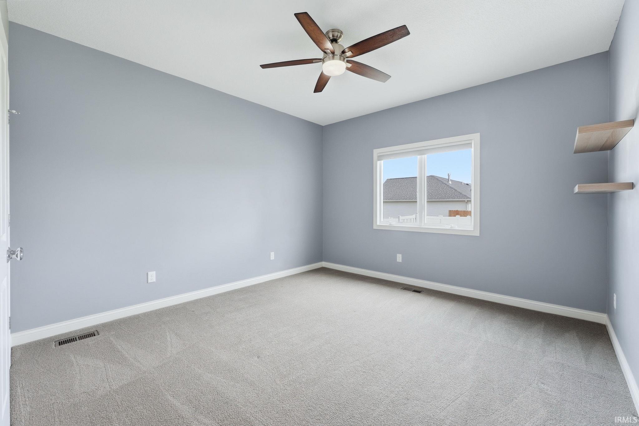 Spacious room featuring vaulted ceilings, light blue walls, carpet flooring, a ceiling fan with integrated lighting, and a window providing natural illumination