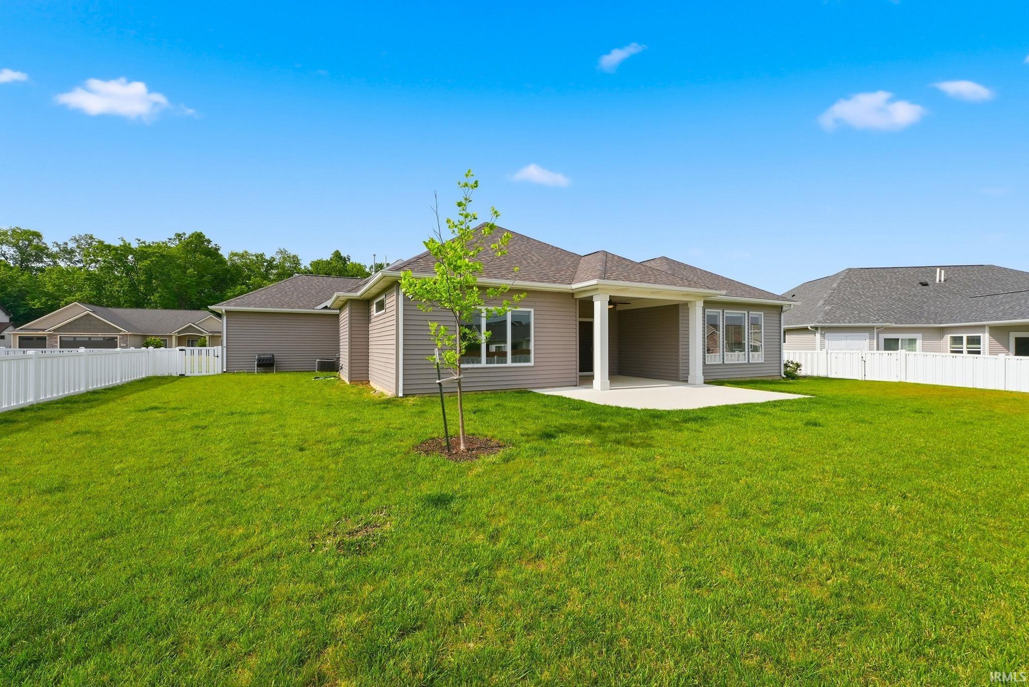 Expansive backyard featuring a manicured lawn, a young deciduous tree, and a white picket fence