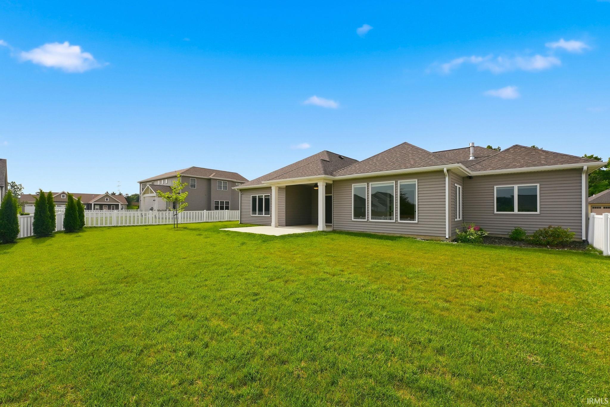Expansive backyard featuring a lush lawn, white picket fencing, and a concrete patio