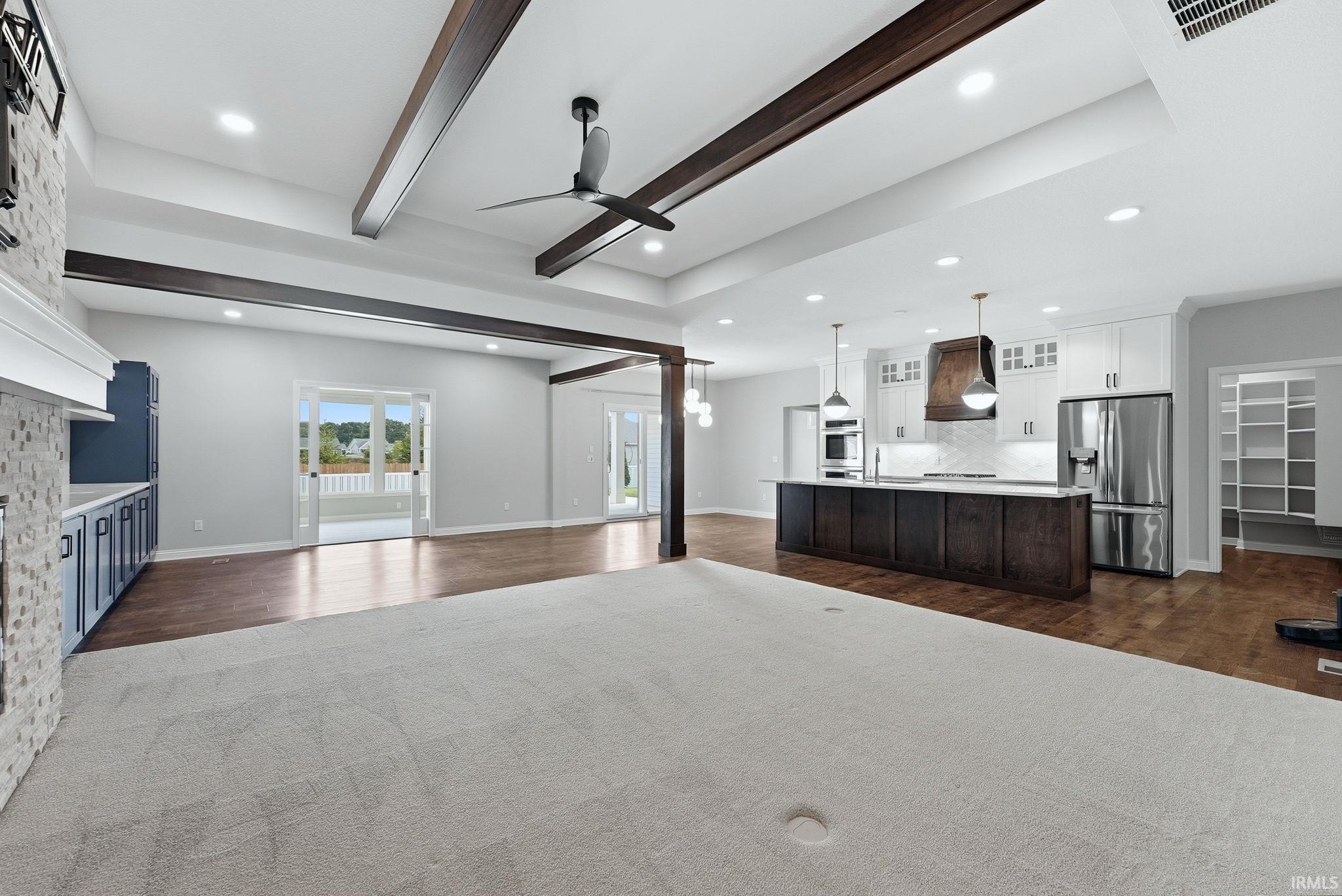 Expansive living area featuring a tray ceiling with dark wood beams, recessed lighting, and a ceiling fan