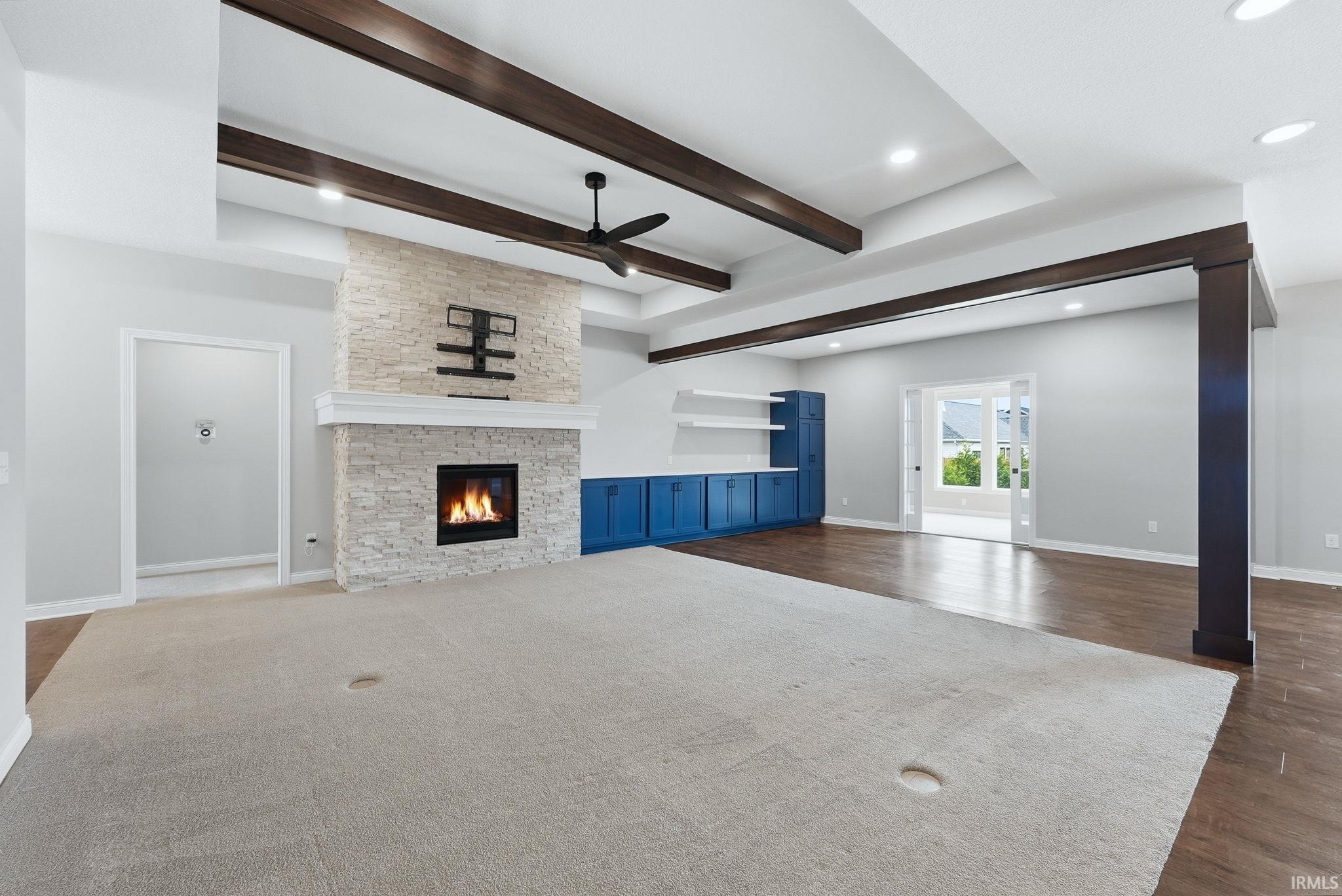 Expansive living area featuring a stacked stone fireplace with a white mantel, exposed wood ceiling beams, and recessed lighting