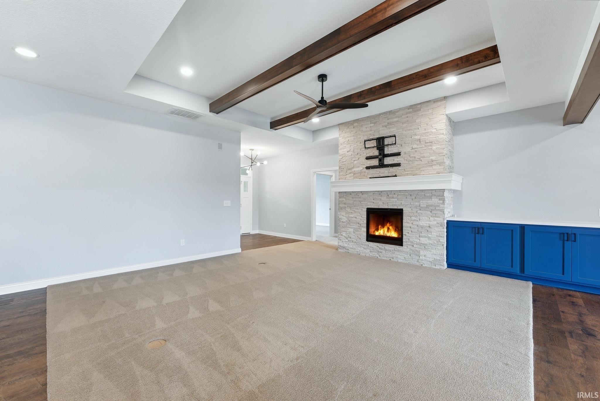 Living area featuring a stone-clad fireplace with a white mantel, wood-finish ceiling beams, and a ceiling fan