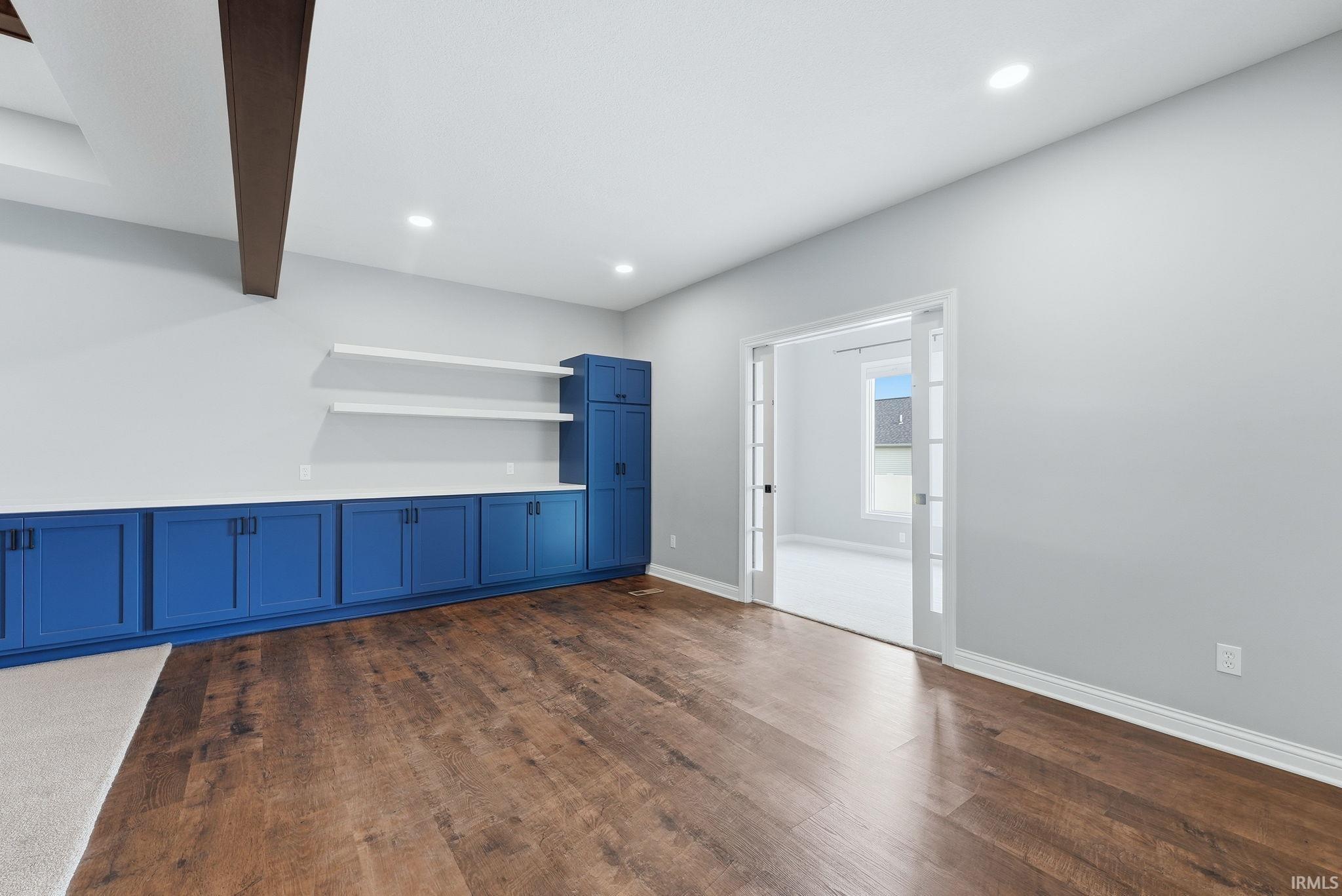 Wood-finish flooring throughout, complemented by a full wall of built-in blue cabinetry with white countertops and floating shelves
