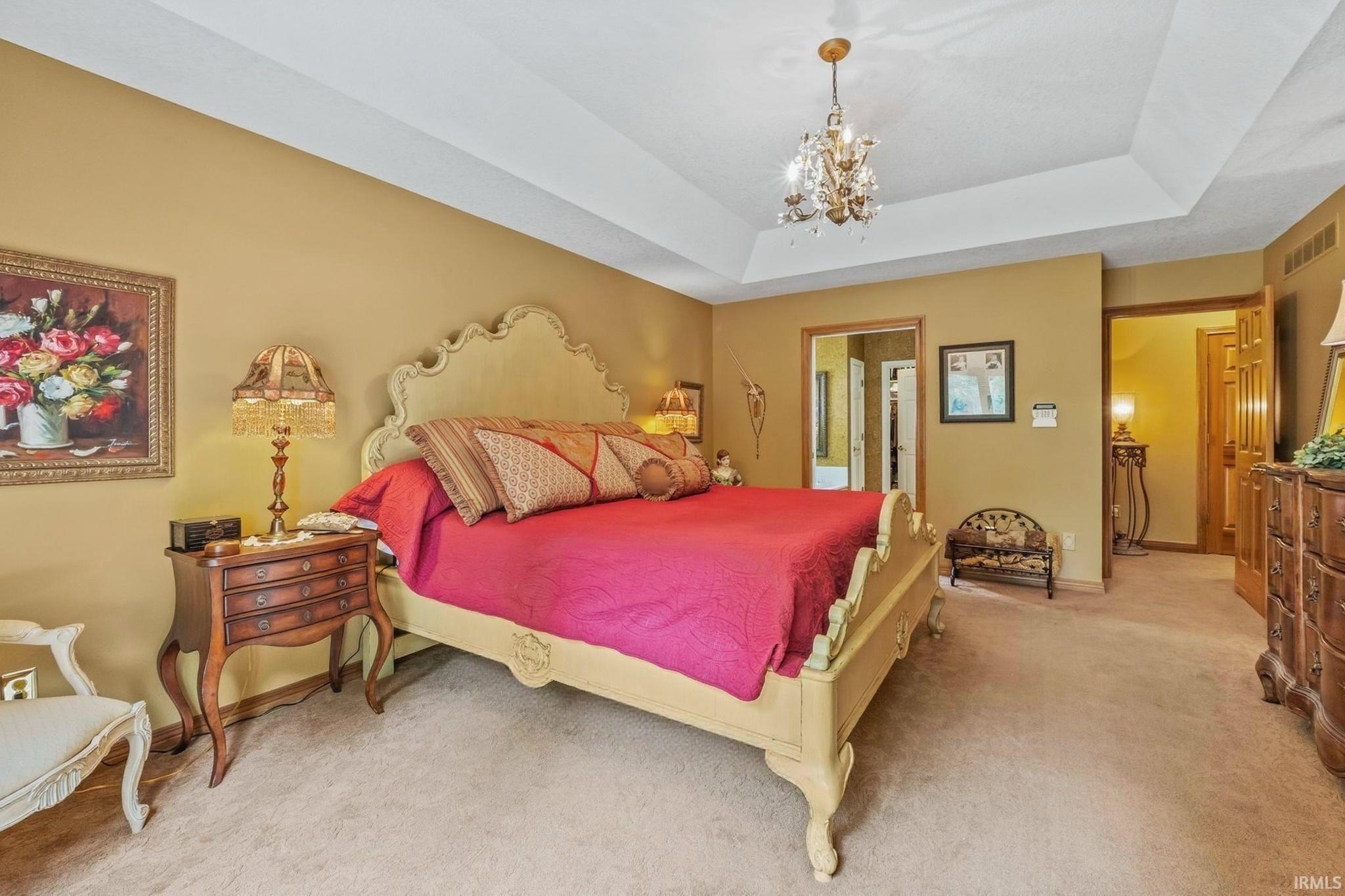 Carpeted bedroom featuring a tray ceiling with a chandelier, warm-toned wall paint, and an arched entryway