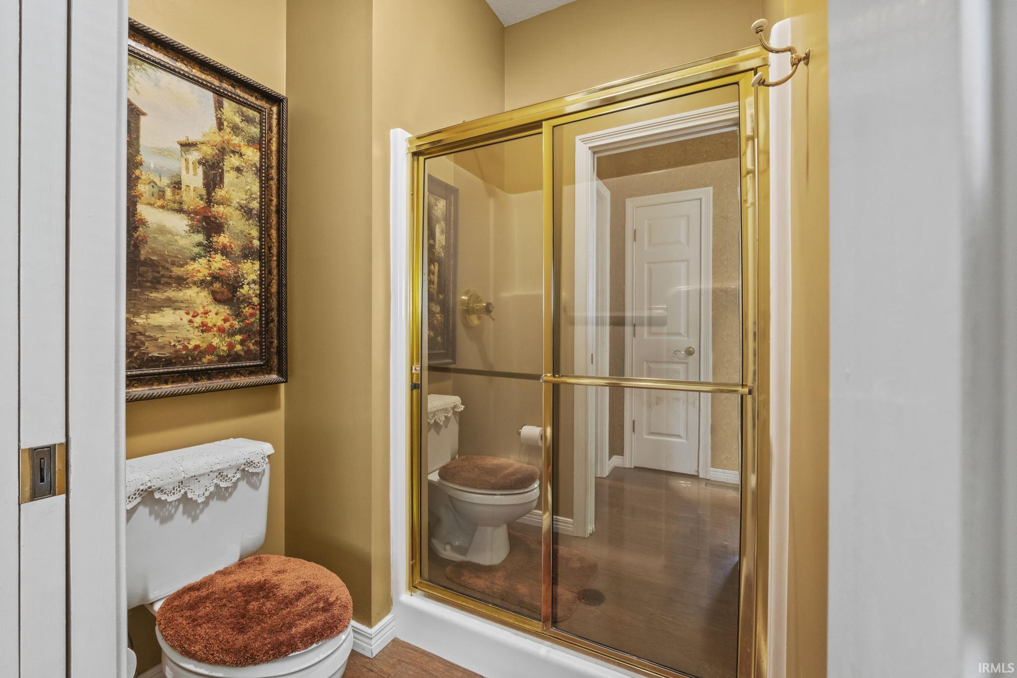 Full bathroom featuring a shower with a brass-finish framed glass enclosure, wood-finish flooring, and a white toilet