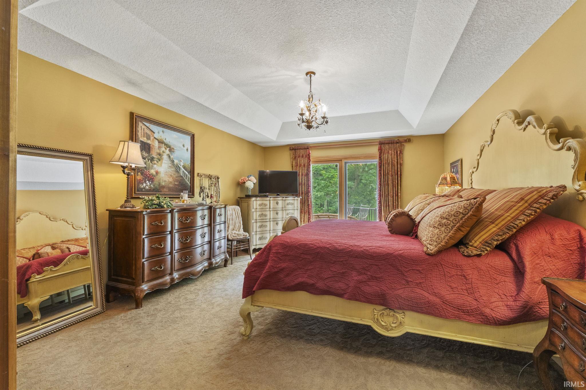 Bedroom featuring a tray ceiling with a chandelier, carpet flooring, and a large window with outdoor scenery
