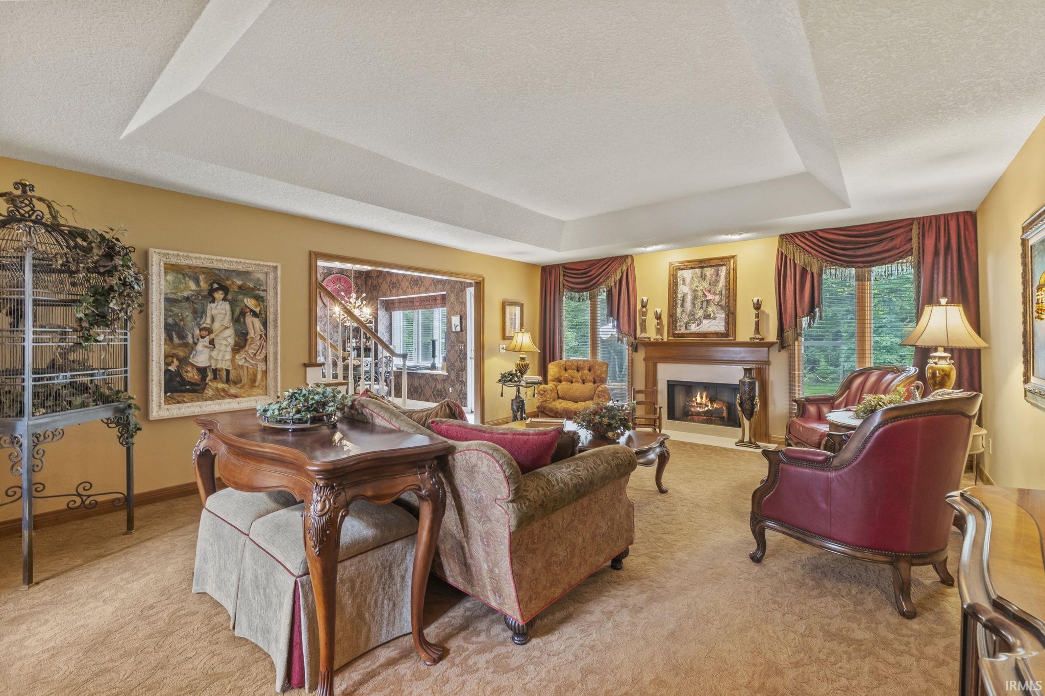 Spacious living area featuring a tray ceiling, a central fireplace with a wood mantle, and multiple windows with drapery