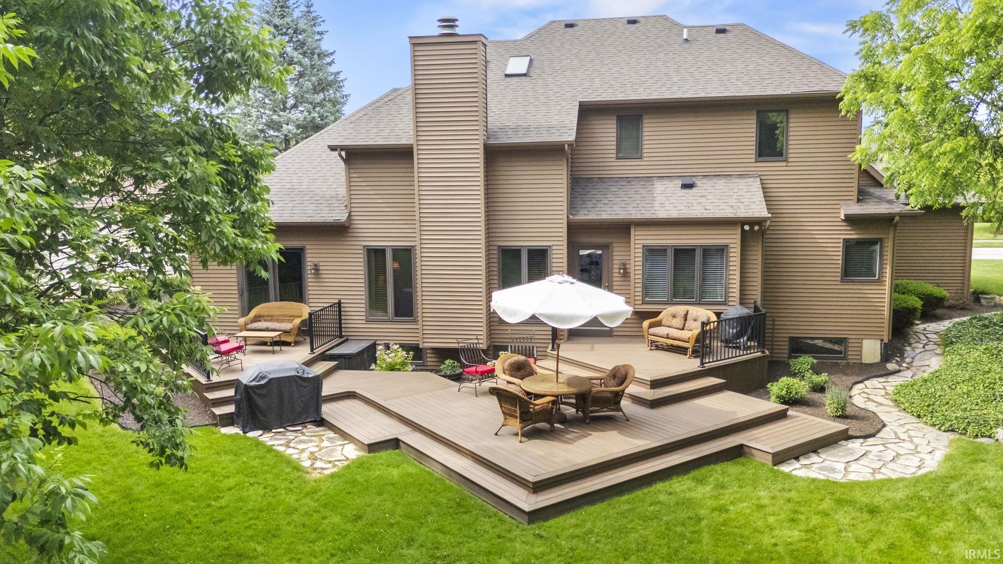 Multi-level composite deck with integrated steps, surrounded by manicured lawn and mature landscaping, featuring a stone path