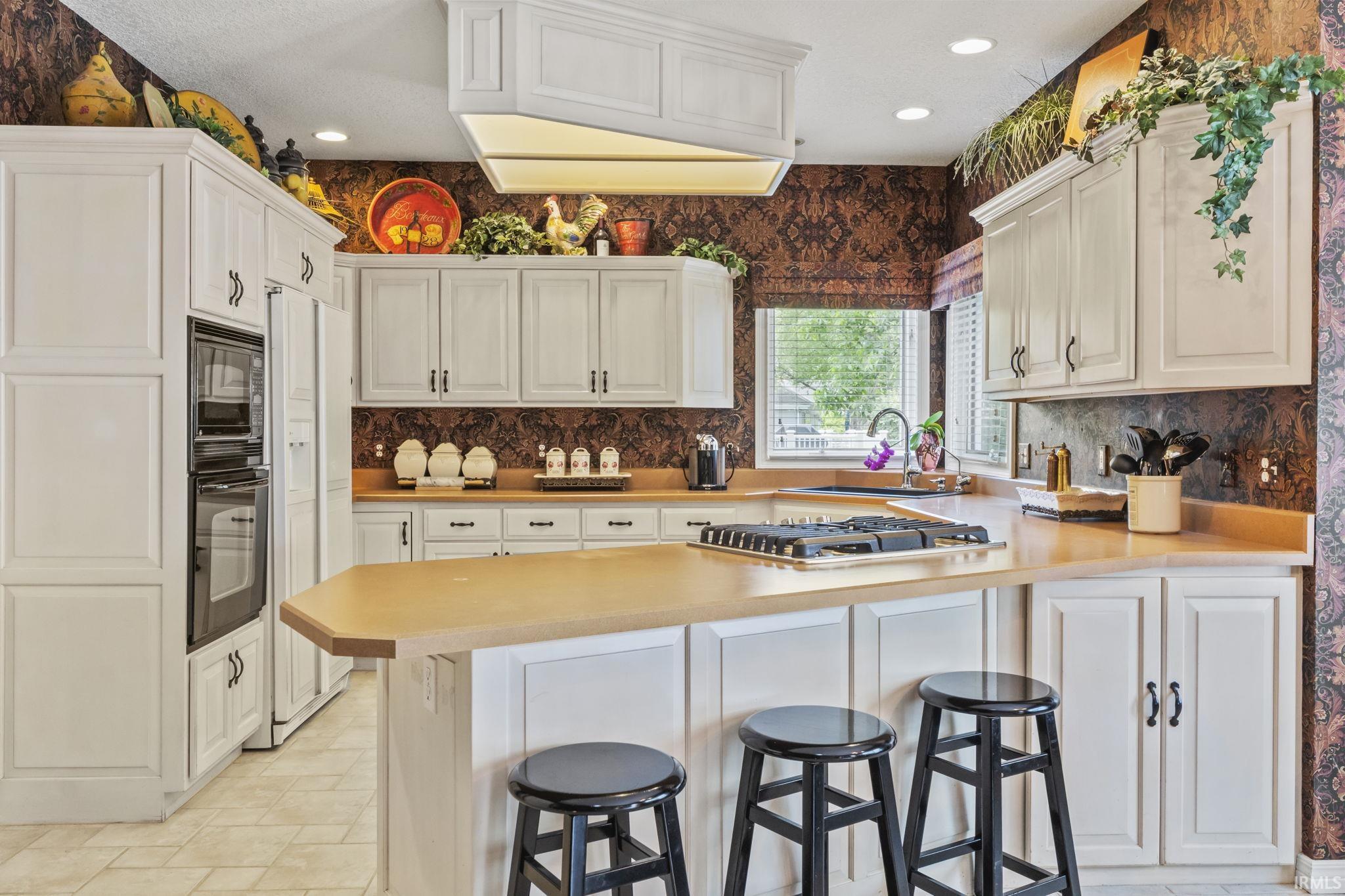 Kitchen featuring white cabinetry, light-toned countertops, a built-in double oven, and a gas cooktop on the island