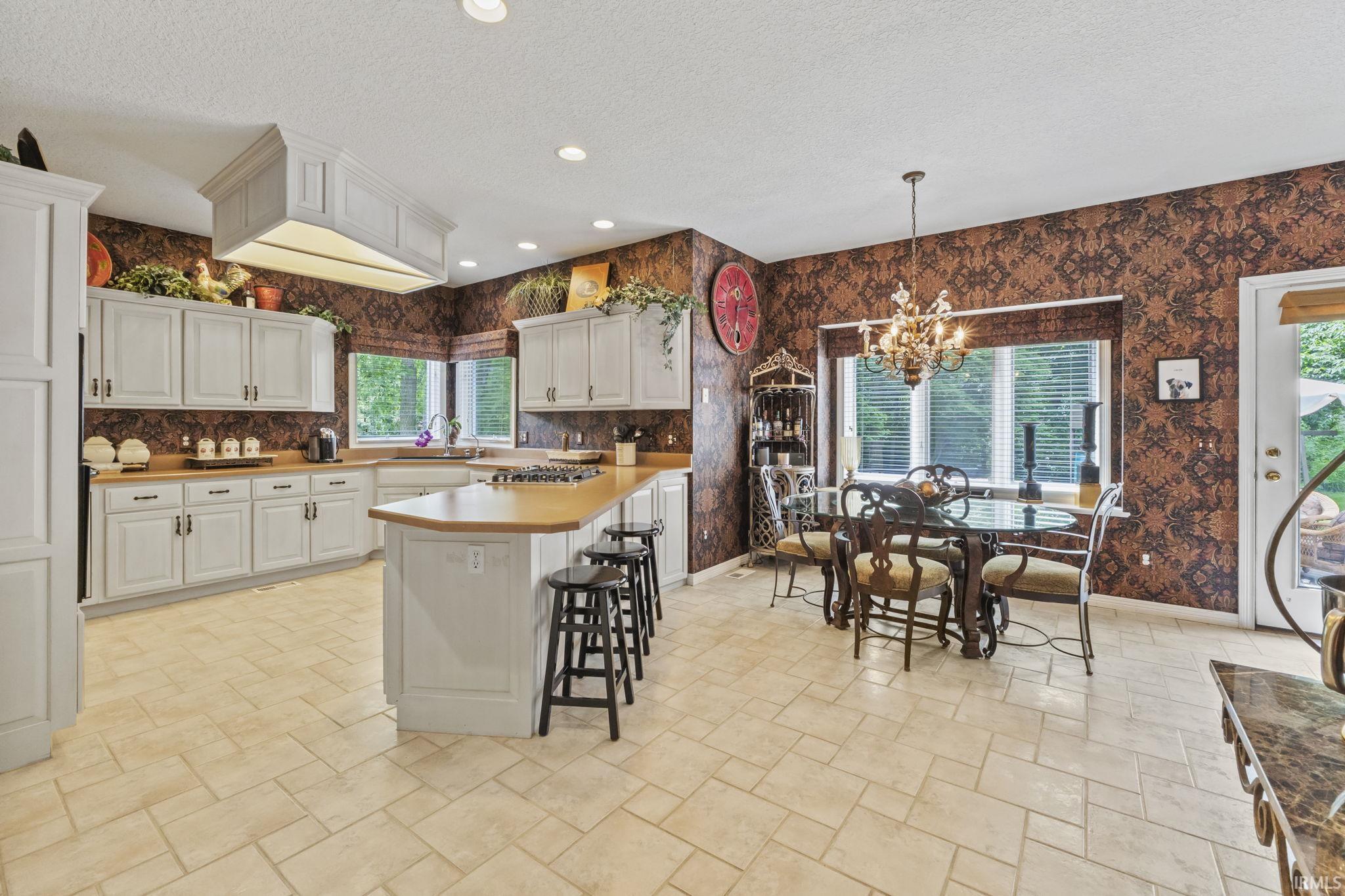 Kitchen and dining area featuring light-toned tile flooring, light-painted cabinetry, wood-finish countertops, a central island with bar seating, and a dining space with a chandelier
