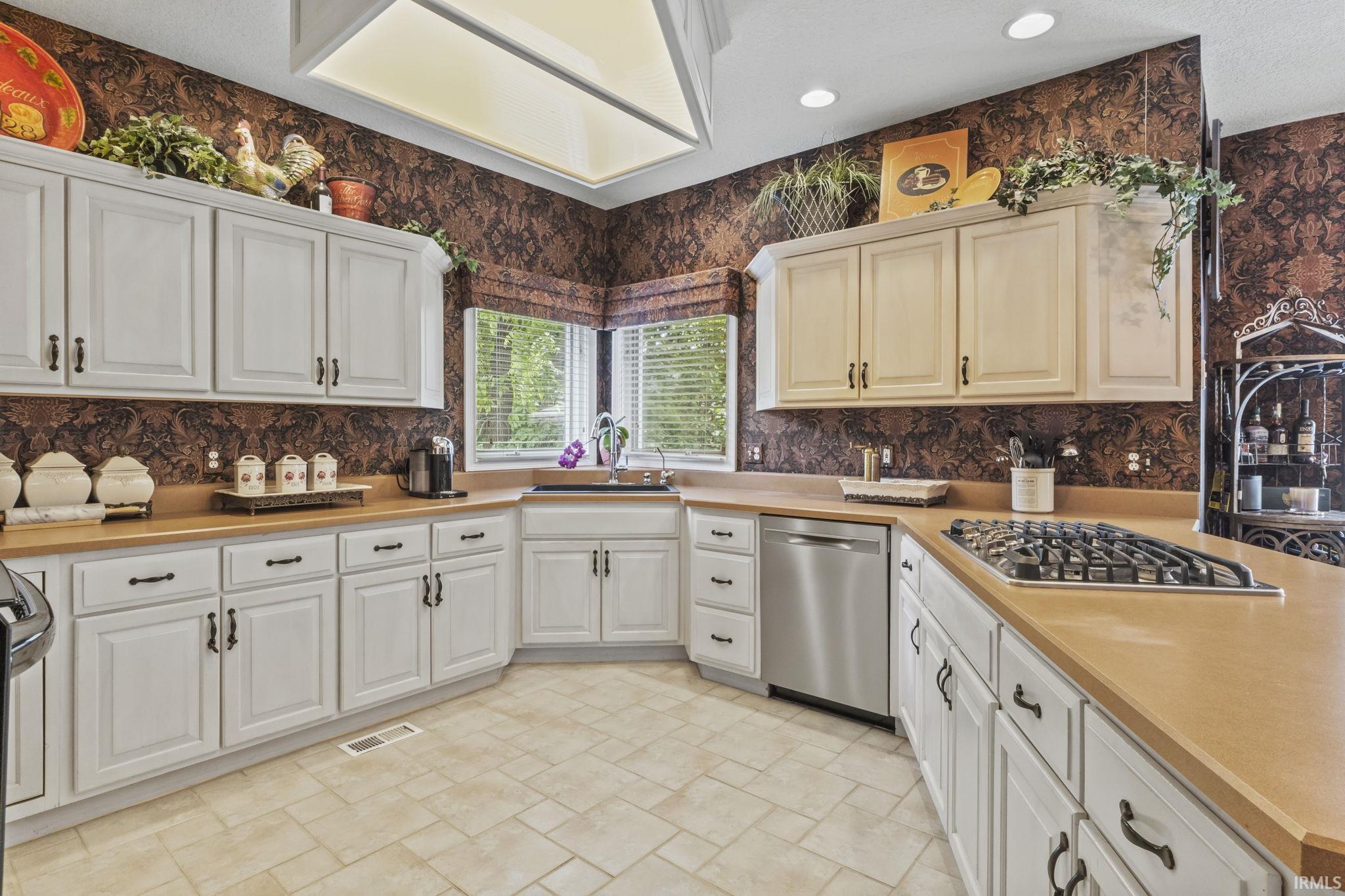 Kitchen featuring white cabinetry with dark hardware, a corner sink with a window, a built-in gas range, stainless steel dishwasher, and tiled flooring