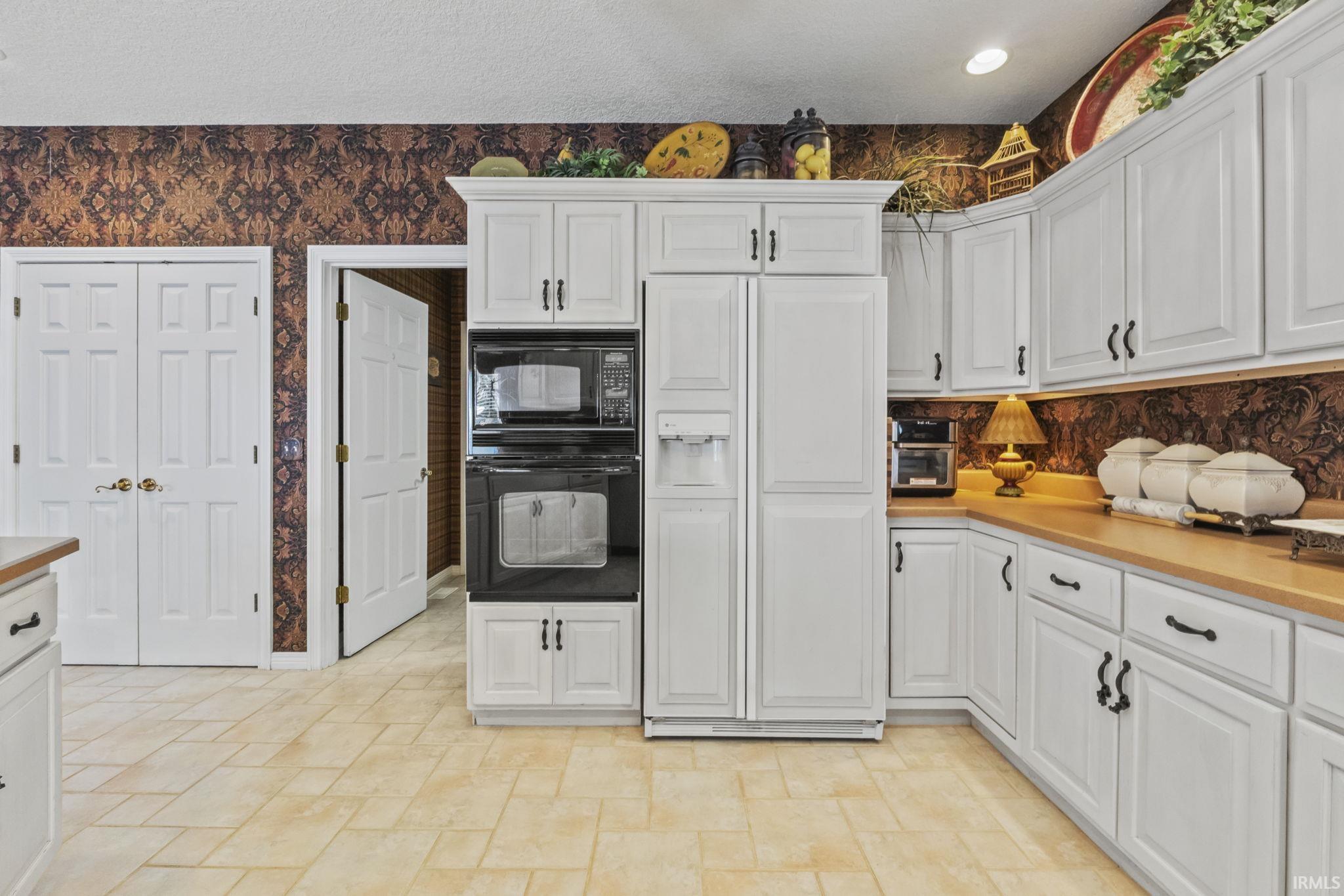 Kitchen featuring extensive white cabinetry with black hardware, built-in microwave, wall oven, and coordinating refrigerator