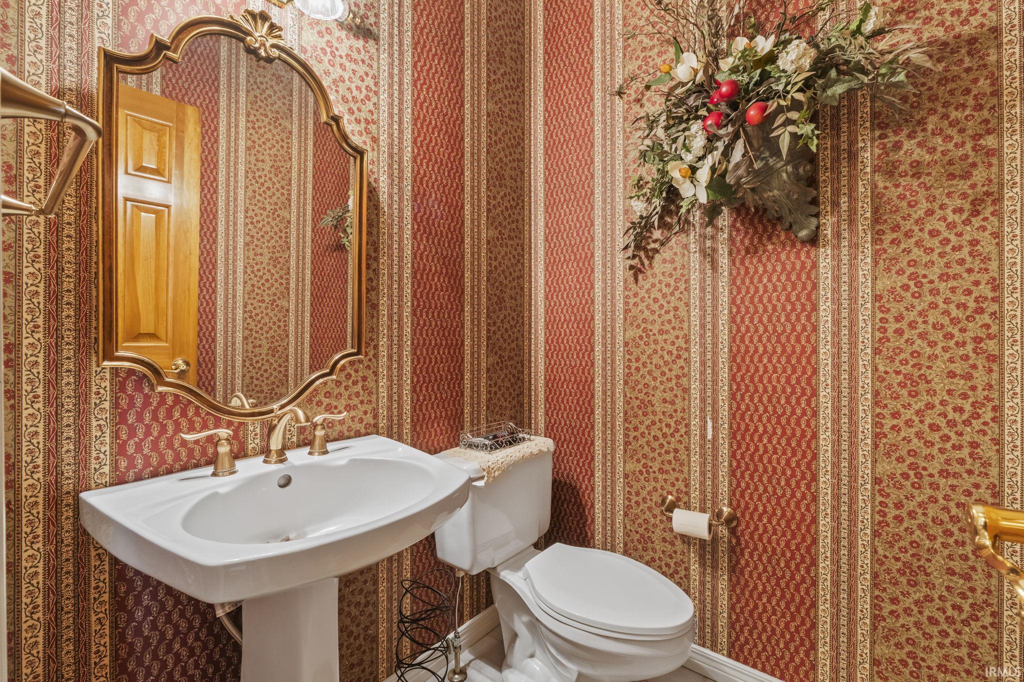 Pedestal sink with brass-finish faucet, ornate framed mirror, and patterned wallpaper