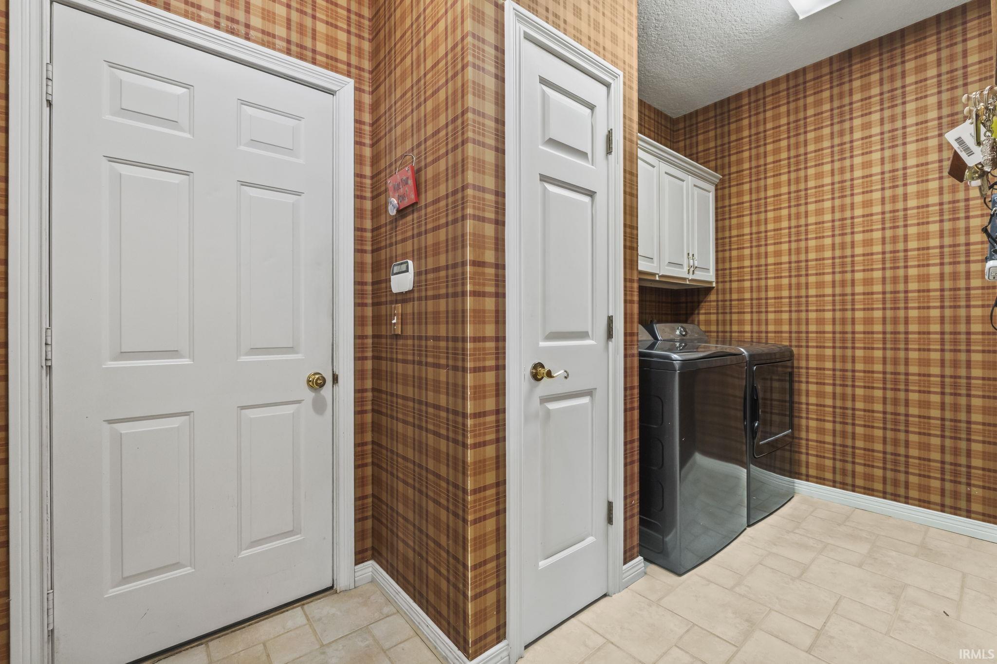 Laundry area with patterned wall covering, two white paneled doors, and light-toned tile flooring