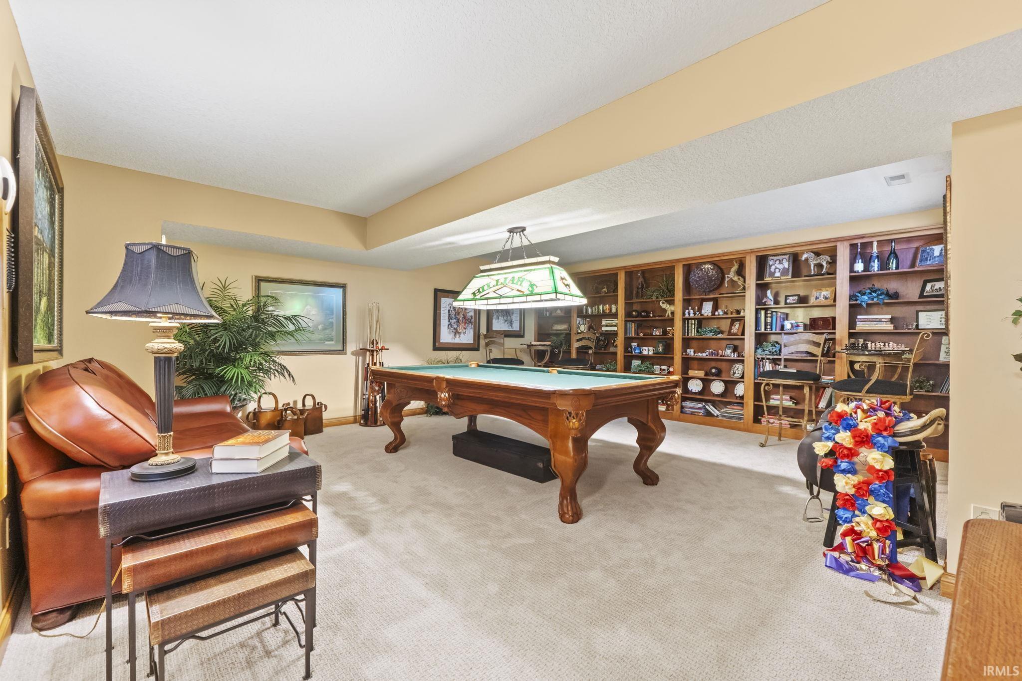 Recessed lighting illuminates a spacious room featuring wall-to-wall carpeting and a substantial built-in wood bookcase system with extensive shelving