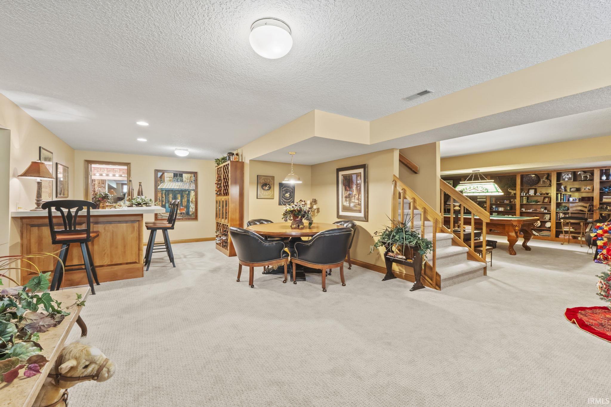 Expansive finished lower level featuring a built-in wet bar with a light wood base and light-toned countertop, recessed lighting, and a broad carpeted area