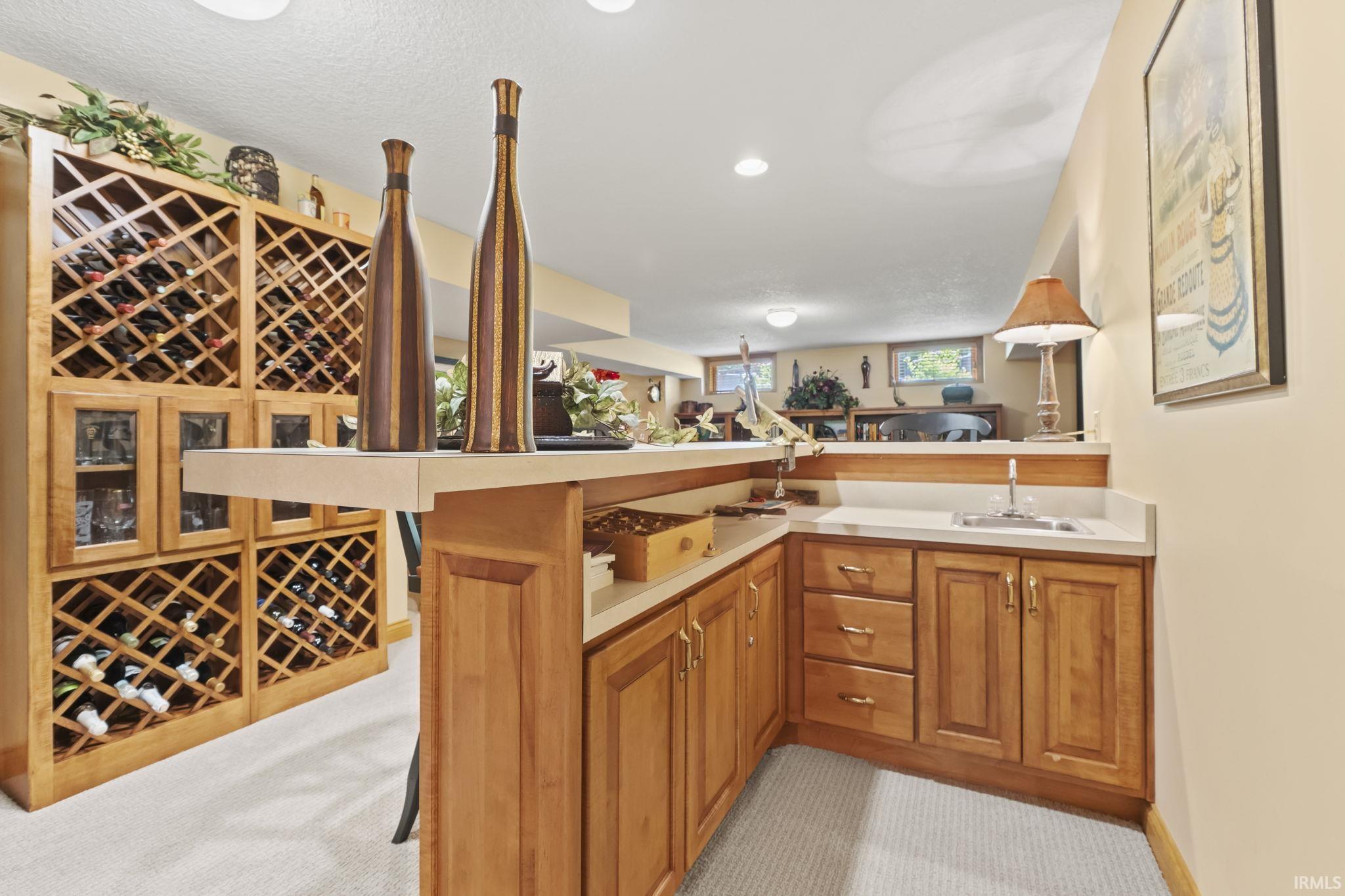 Custom built-in wood wine storage with glass-front display cabinetry, featuring an L-shaped wet bar with a countertop sink and coordinating wood cabinetry