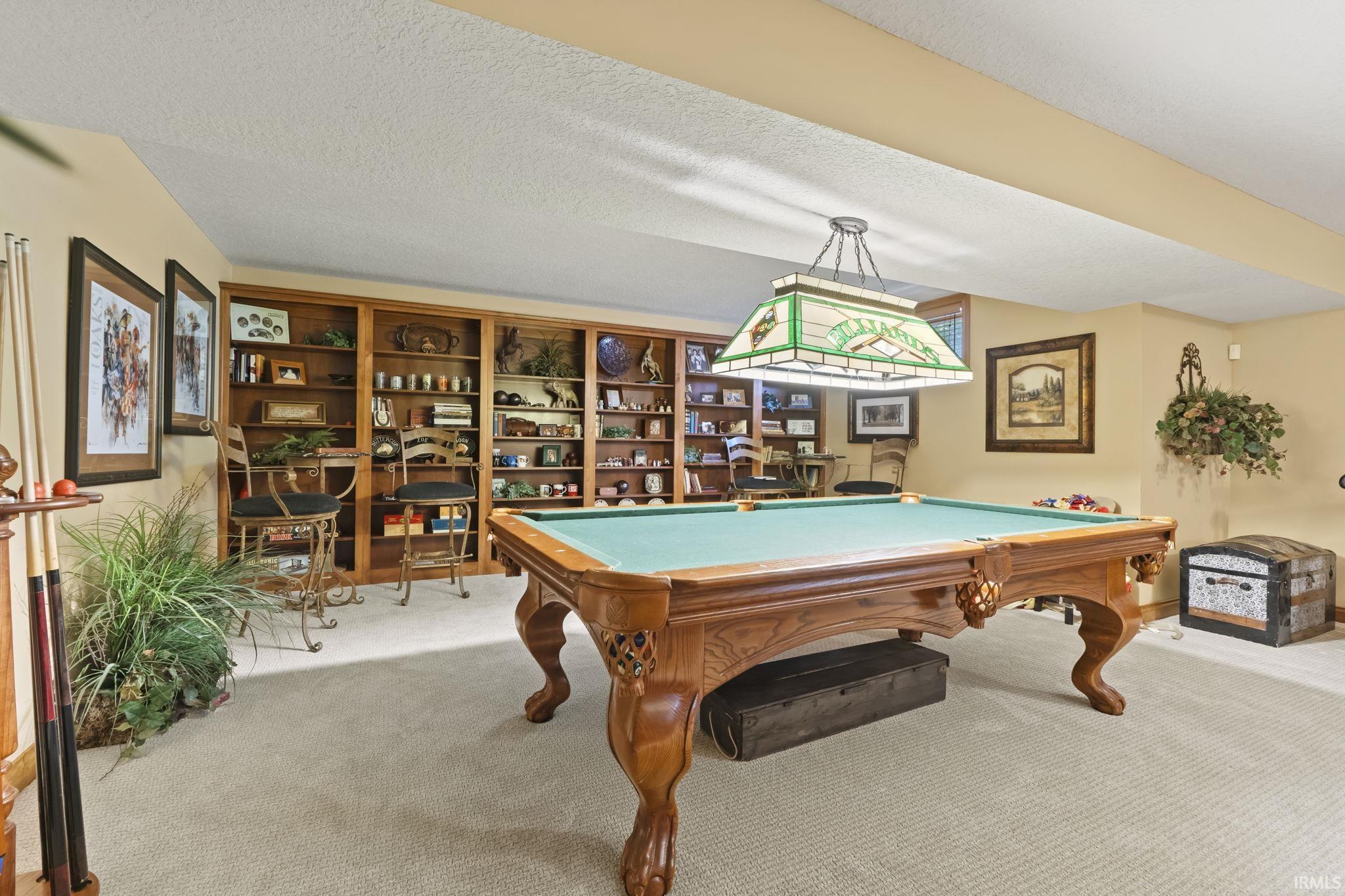 Recreation room with a pool table, wall-to-wall carpeting, extensive built-in wooden shelving, and a Tiffany-style pendant light fixture