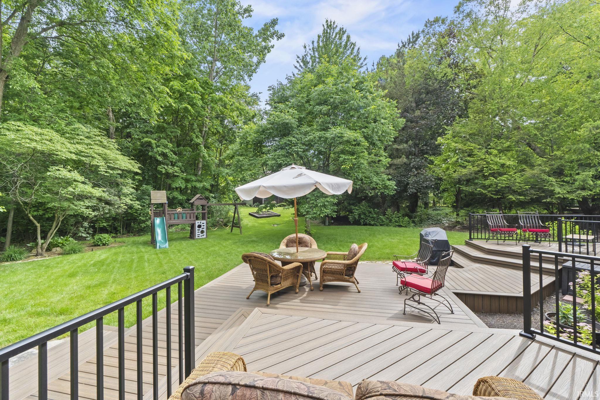 Multi-level composite deck with black metal railings overlooking a private, tree-lined backyard with a spacious lawn
