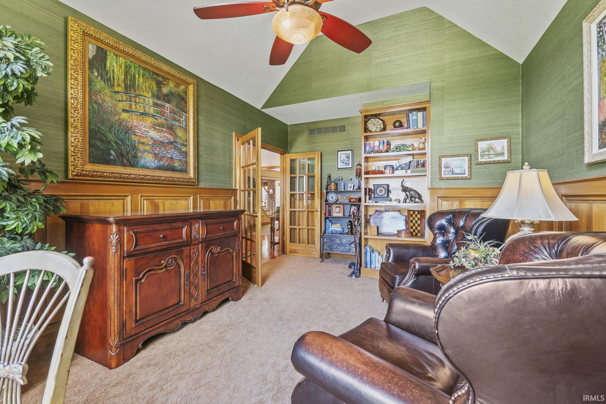 Interior room featuring vaulted ceilings, textured wall finishes, wood paneling, and an integrated ceiling fan