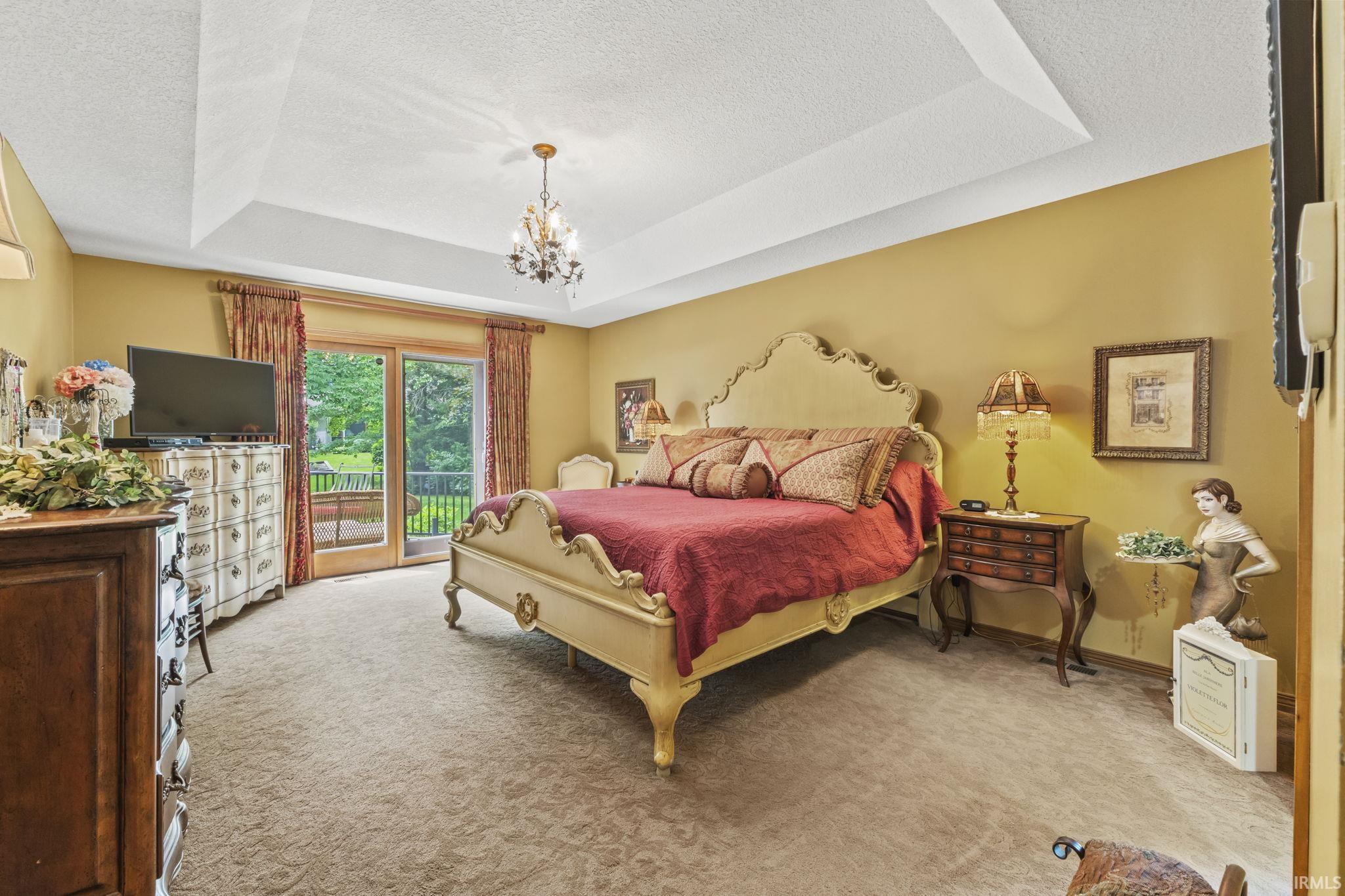 Bedroom featuring a tray ceiling with a chandelier, carpet flooring, and a sliding glass door opening to an outdoor deck