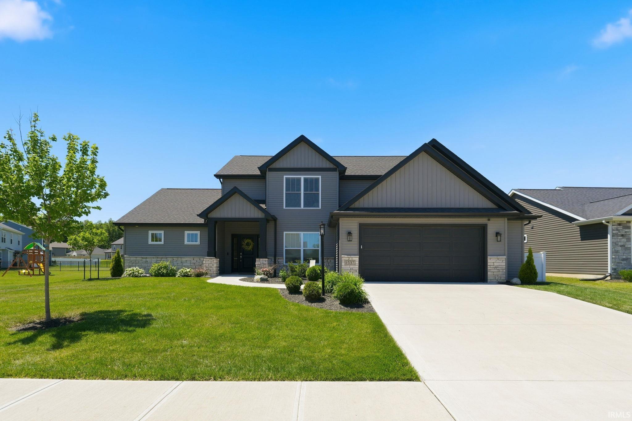 Contemporary two-story home featuring a grey facade with stone accents, a dark roof, and a two-car garage
