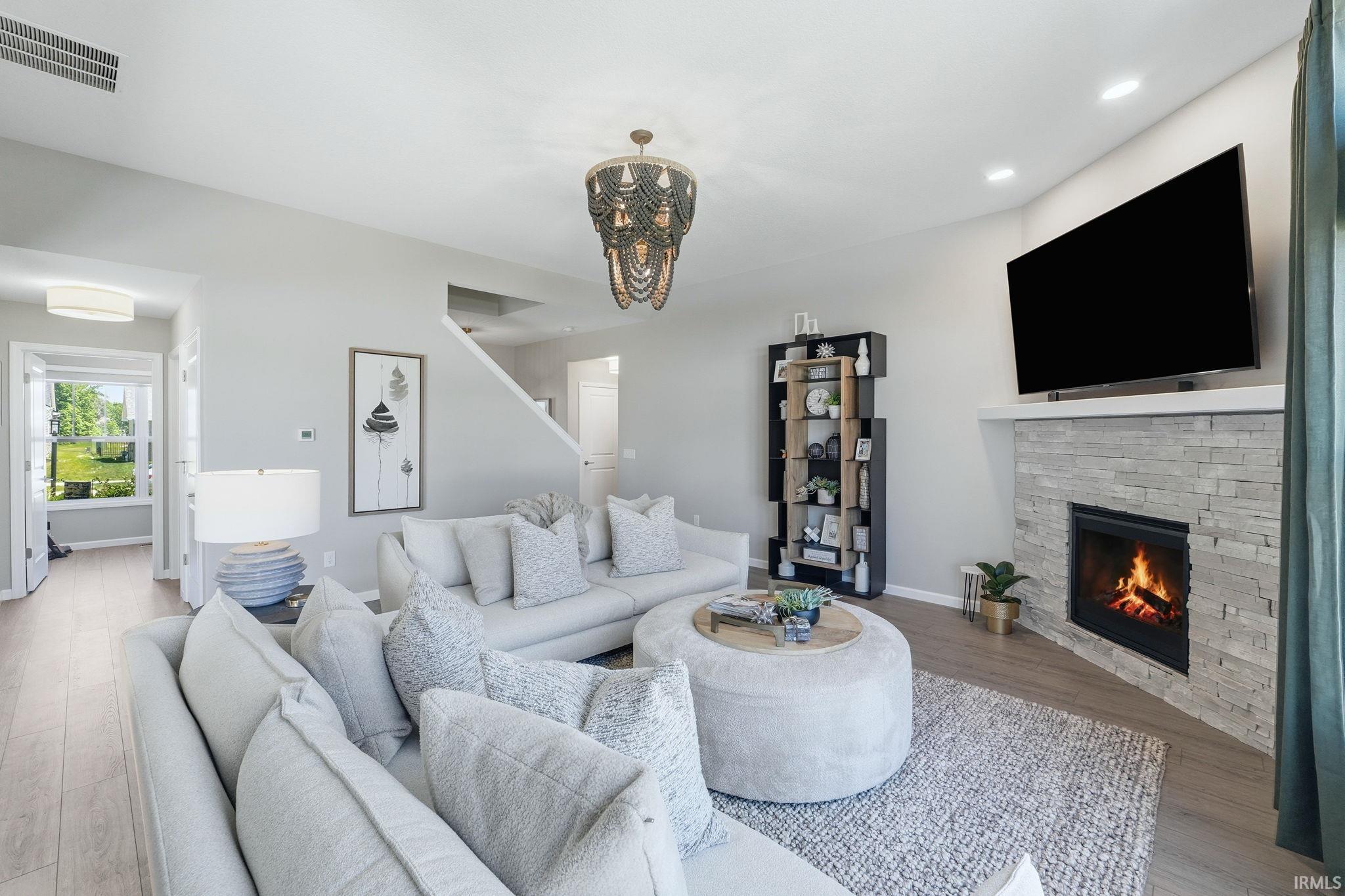 Spacious living area featuring light wood-finish flooring and a corner fireplace with a stone surround