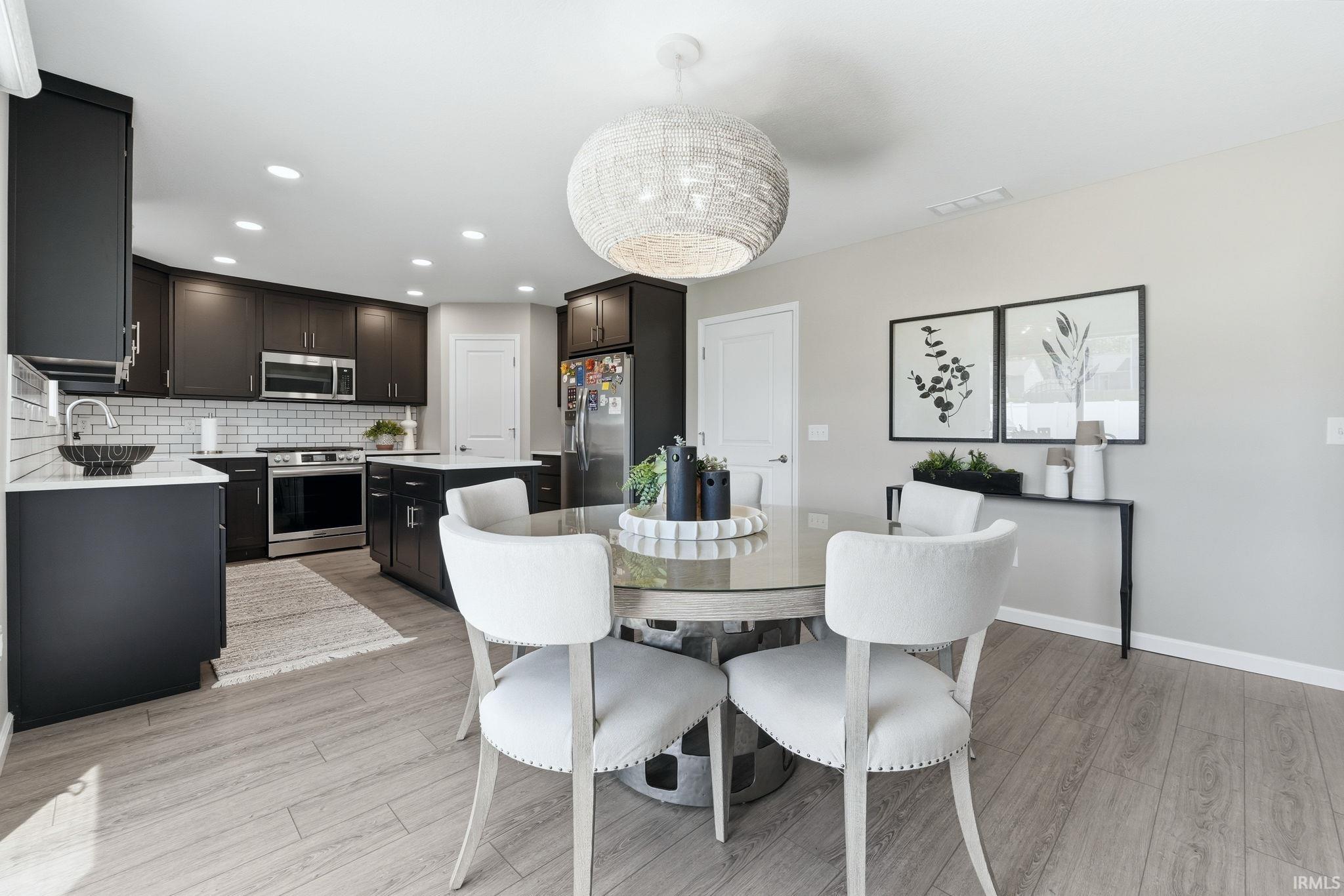 Open-concept kitchen and dining area featuring wood-finish flooring, recessed lighting, and a woven pendant light fixture