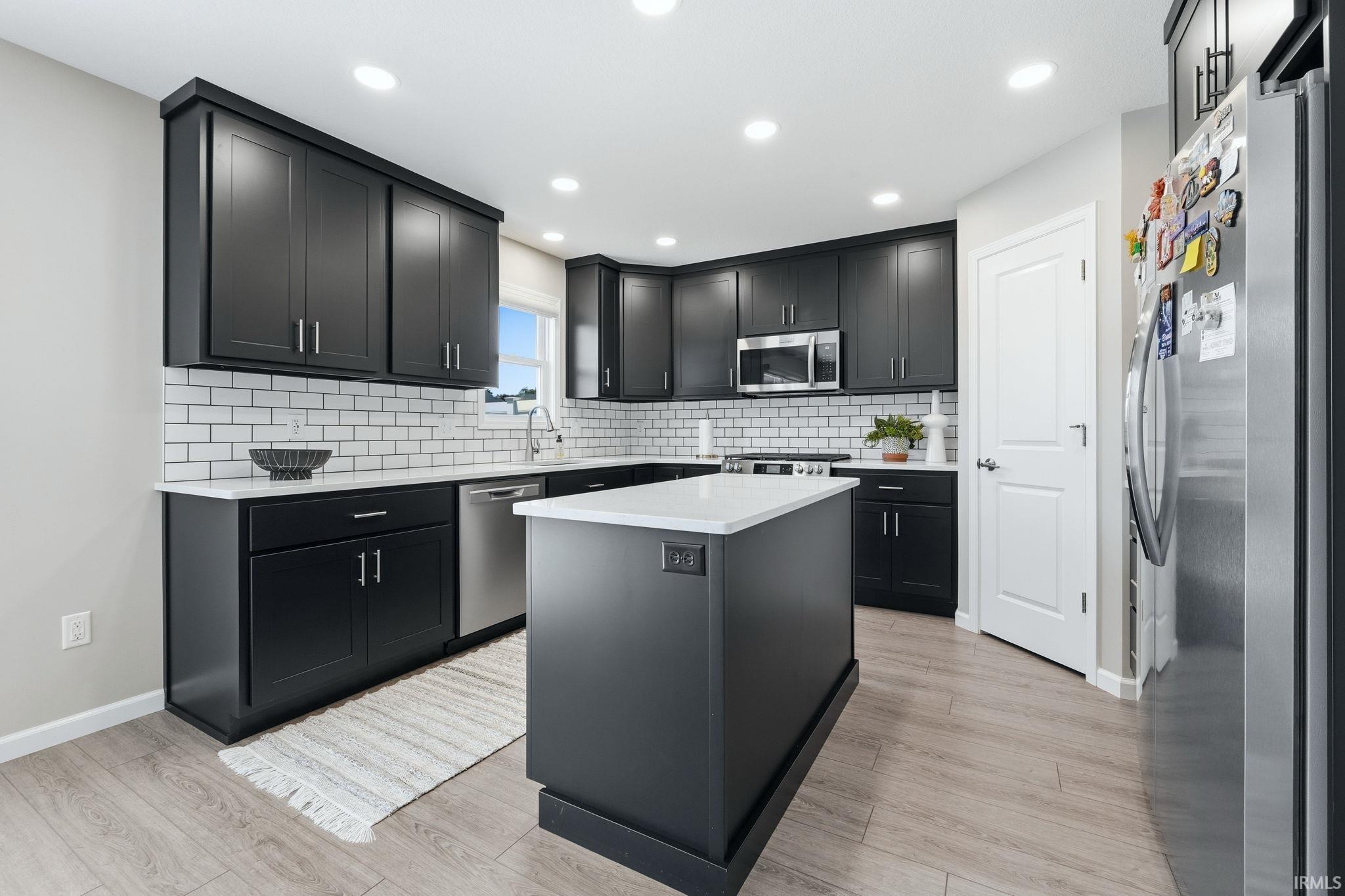 Kitchen featuring dark cabinetry, white subway tile backsplash, light stone countertops, a center island, and wood-finish flooring