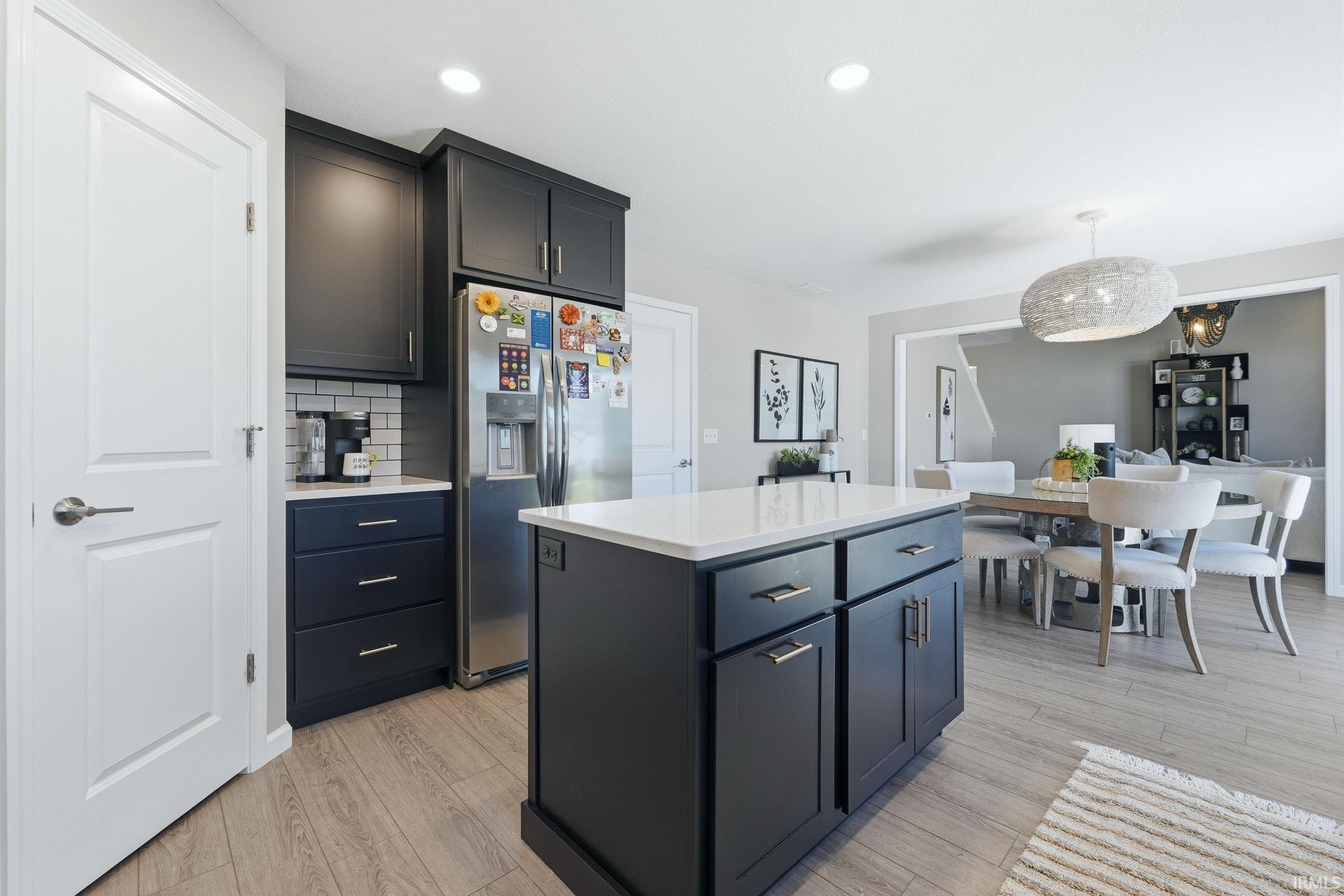 Modern kitchen featuring dark cabinetry, a white countertop island, wood-finish flooring, recessed lighting, and a subway tile backsplash