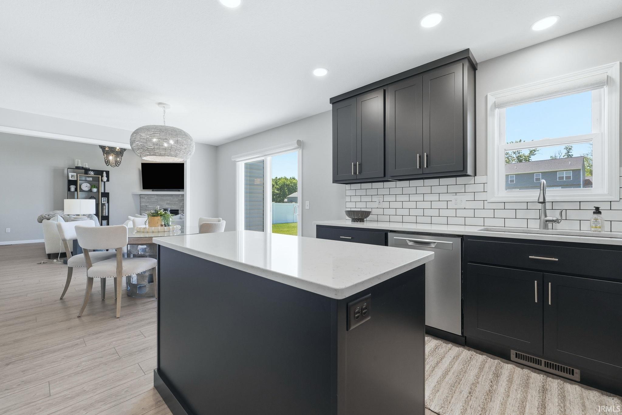 Modern kitchen featuring dark cabinetry, white subway tile backsplash, and a central island with a white countertop