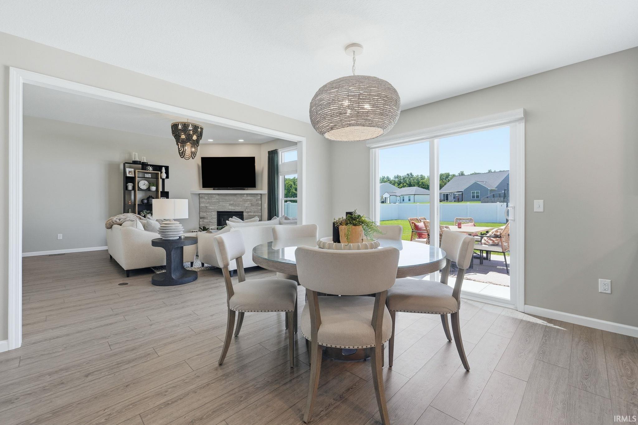 Open-concept living space featuring wood-finish flooring, a contemporary dining area with a woven pendant light, and sliding glass doors leading to a patio