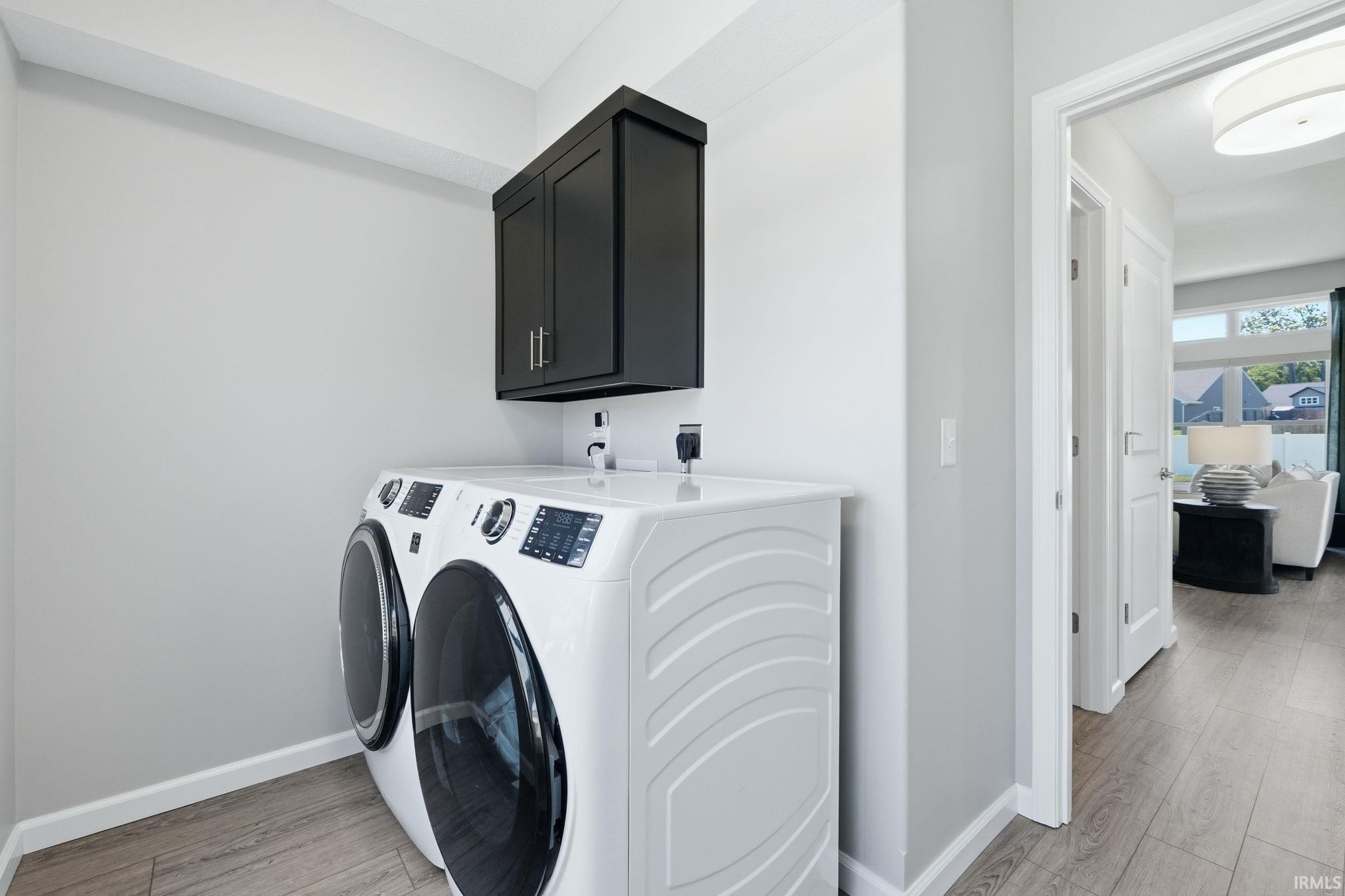 Laundry area featuring wood-finish flooring, white baseboards, and a dark wall-mounted cabinet with silver hardware