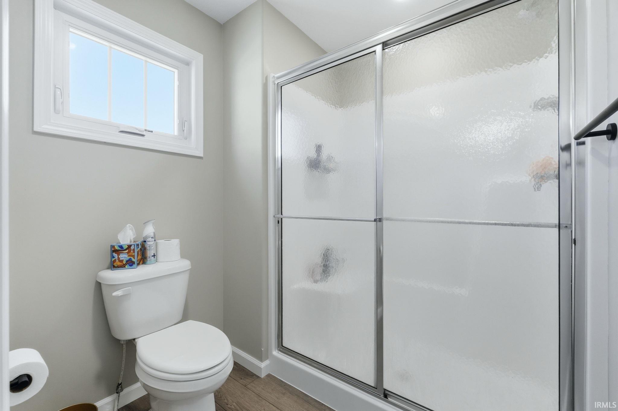 Bathroom featuring a white toilet, framed window, and a shower with sliding textured glass doors and chrome hardware