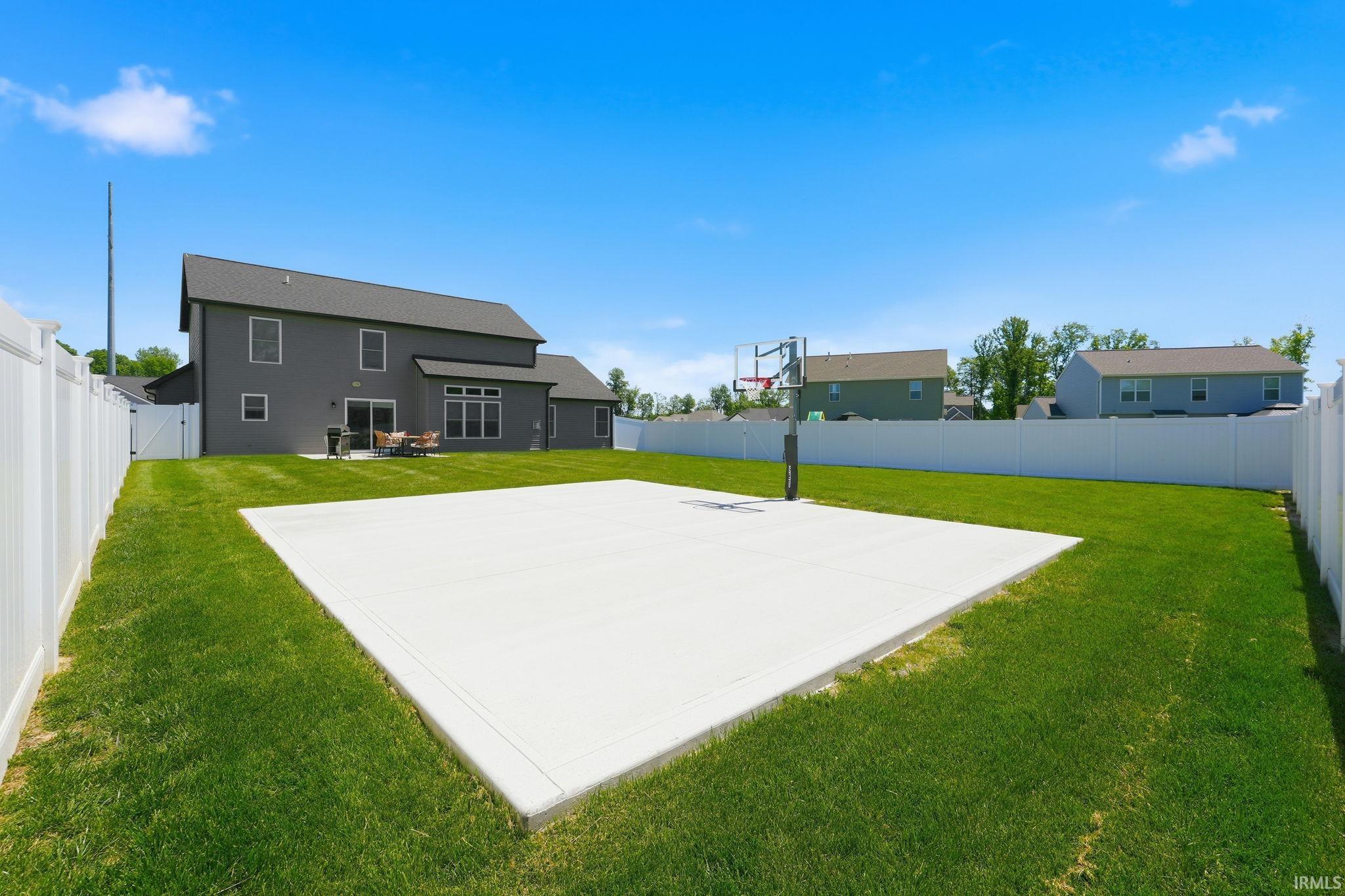 Spacious backyard featuring a large concrete sport court with a basketball hoop, surrounded by a white vinyl fence