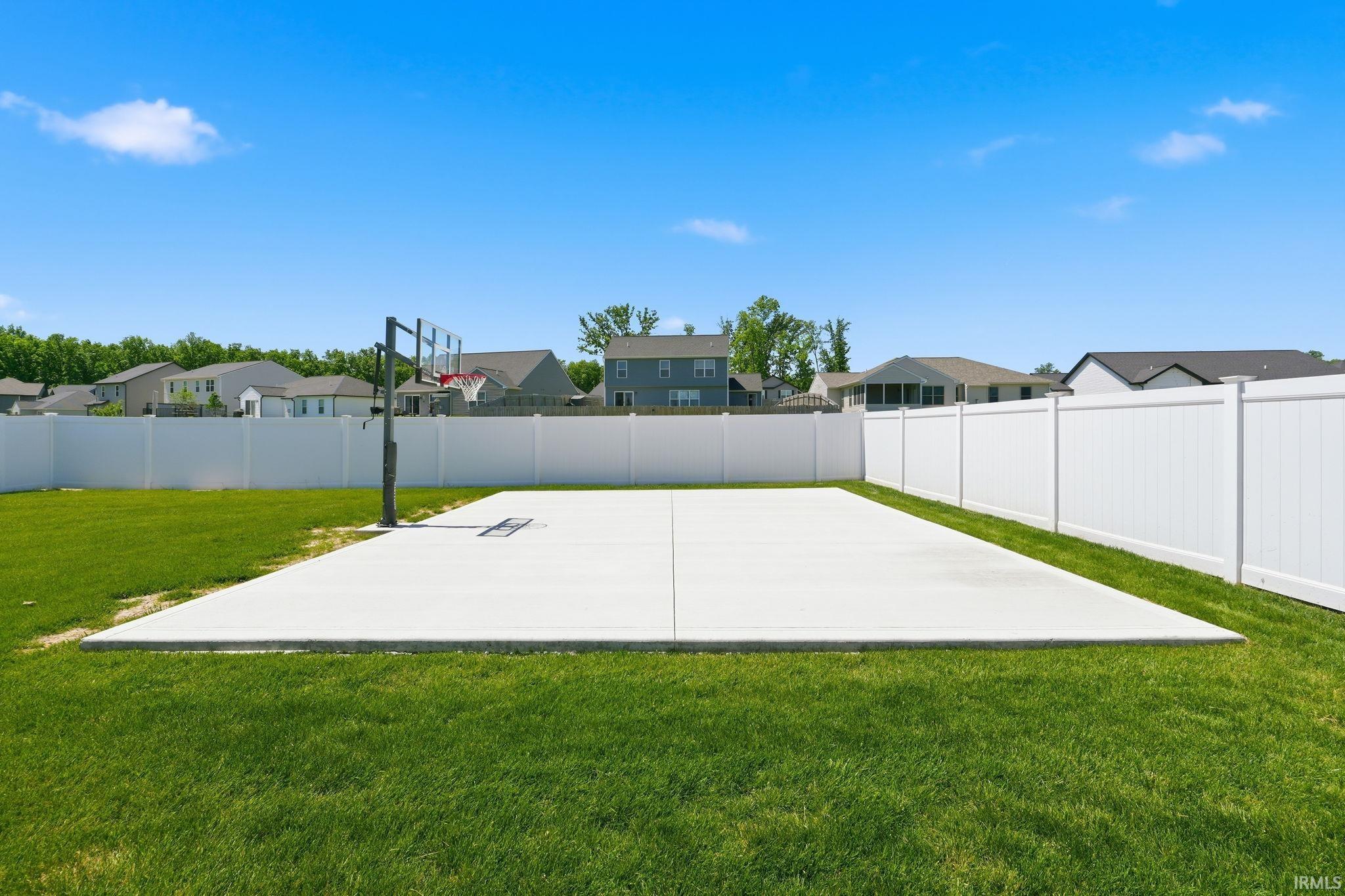 Expansive backyard featuring a concrete sports court with a basketball hoop, surrounded by a white privacy fence