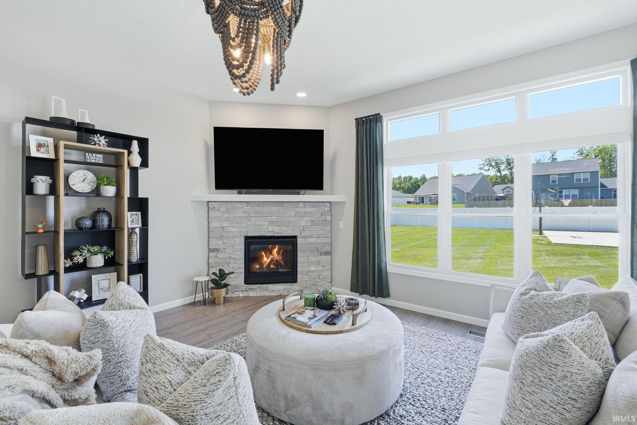 Spacious living area featuring a stacked stone fireplace with a white mantel, an ornate chandelier, large picture windows, wood-finish flooring, and a built-in shelving unit