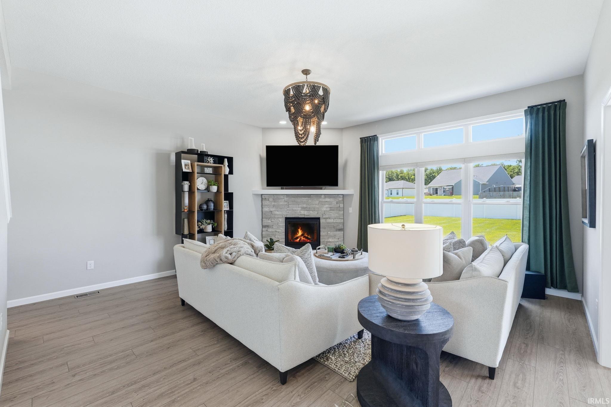 Spacious living area featuring expansive windows, a fireplace with a stone surround, and wood-finish flooring